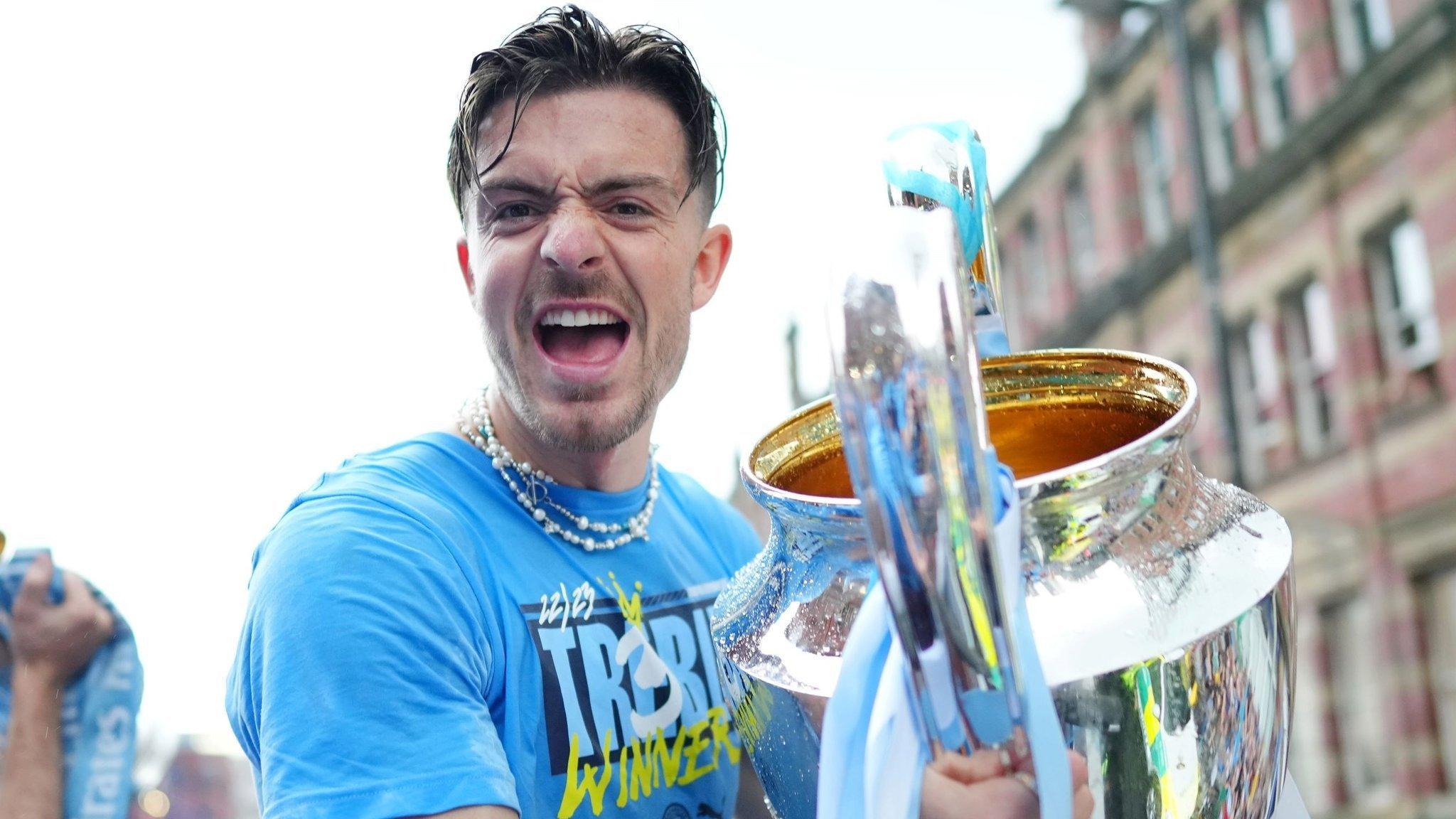 Jack Grealish holds the Champions League trophy on top of an open-top bus