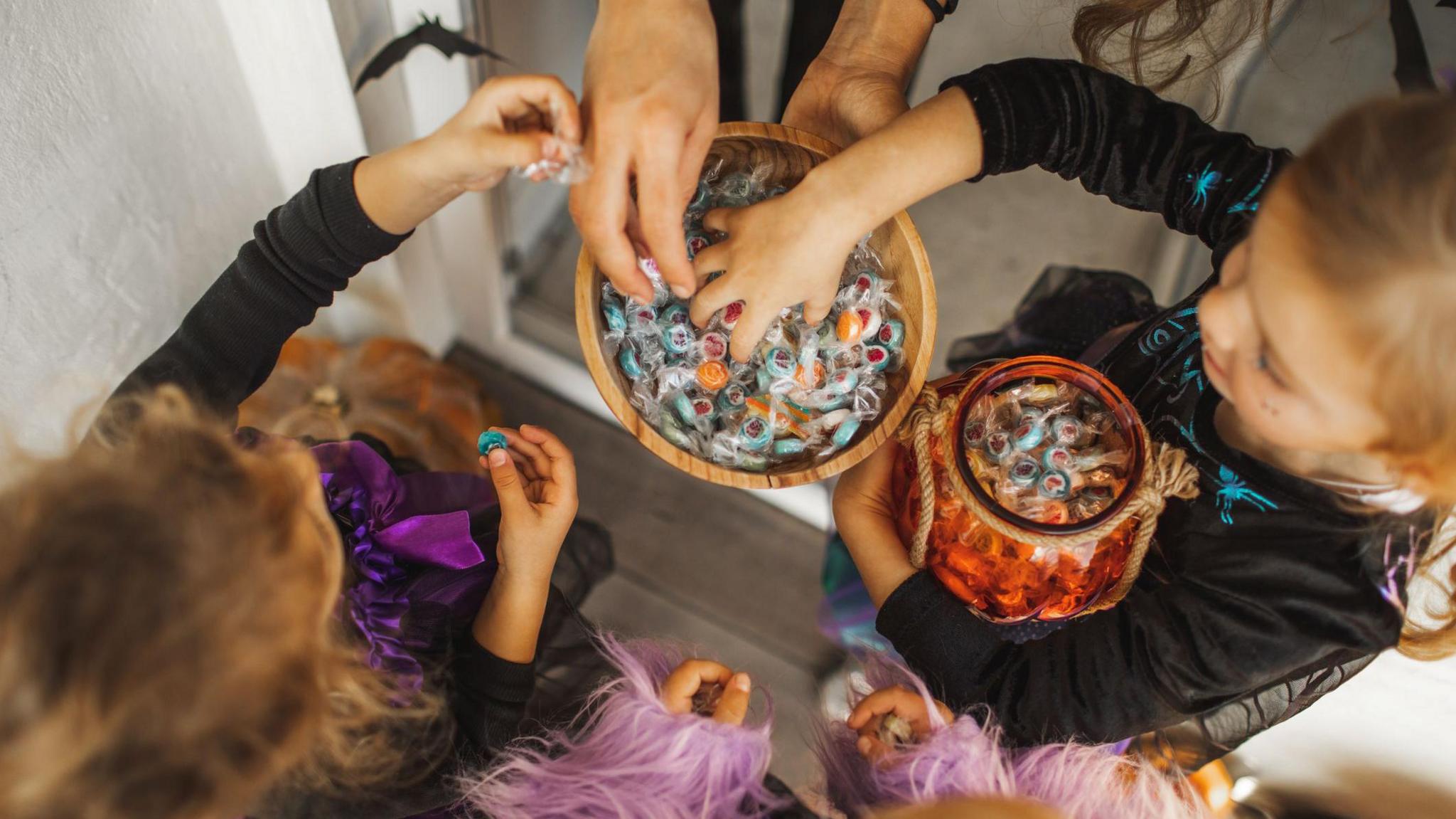 A group of children dressed in black costumes take sweets from a bucket 