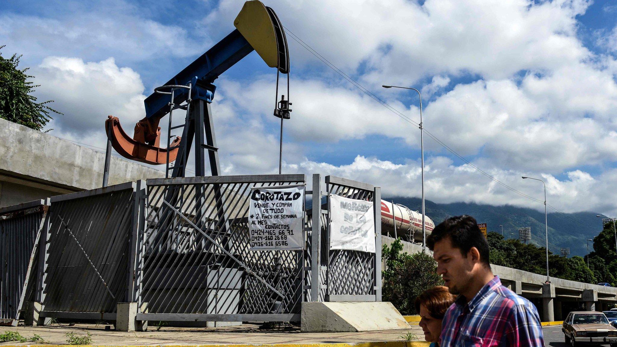 People walk by oil pump in Caracas on November 14, 2017