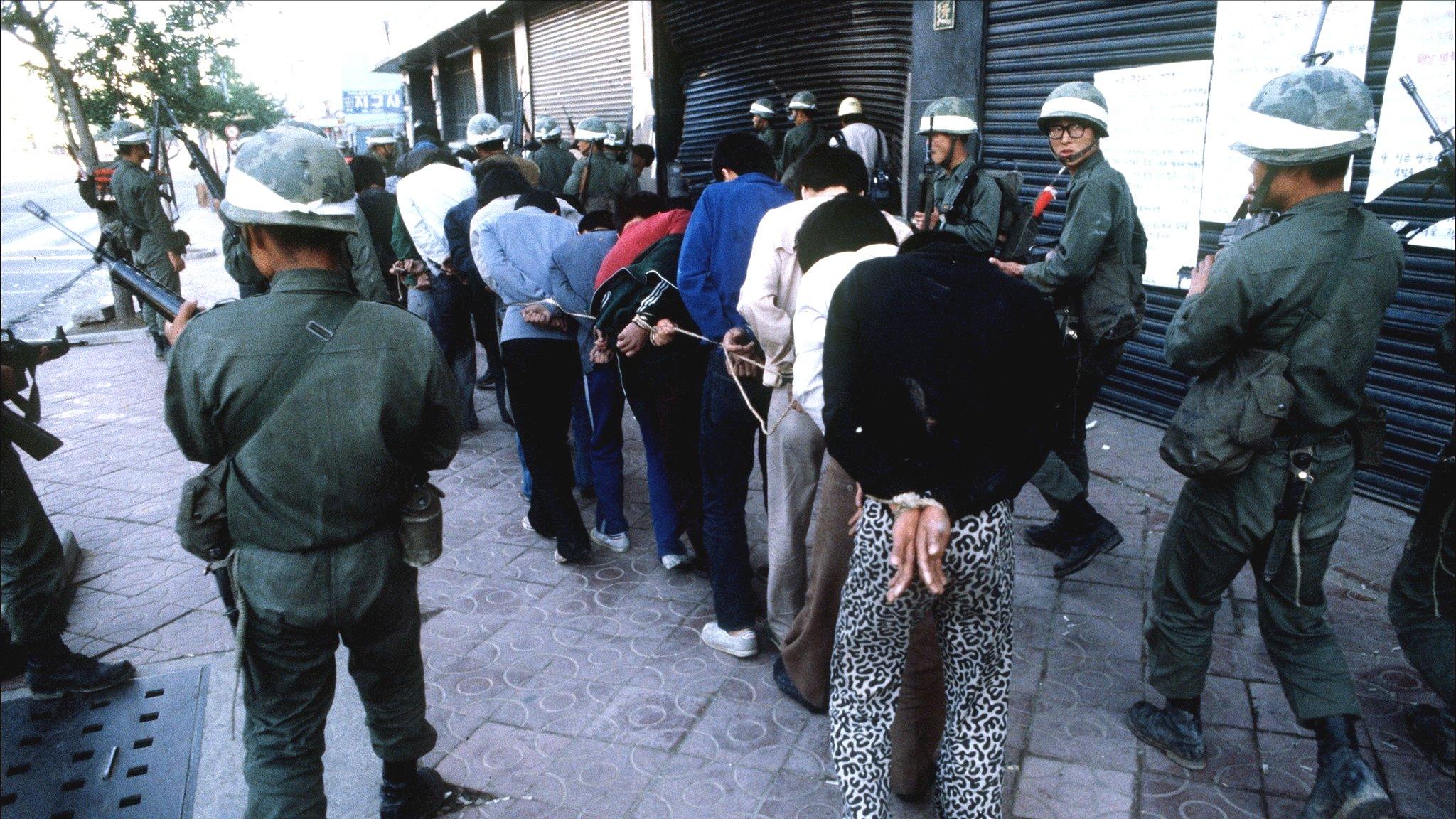 Young students bound together with rope by their hands are led through the streets by soldiers of the Chun Doo-hwan dictatorship