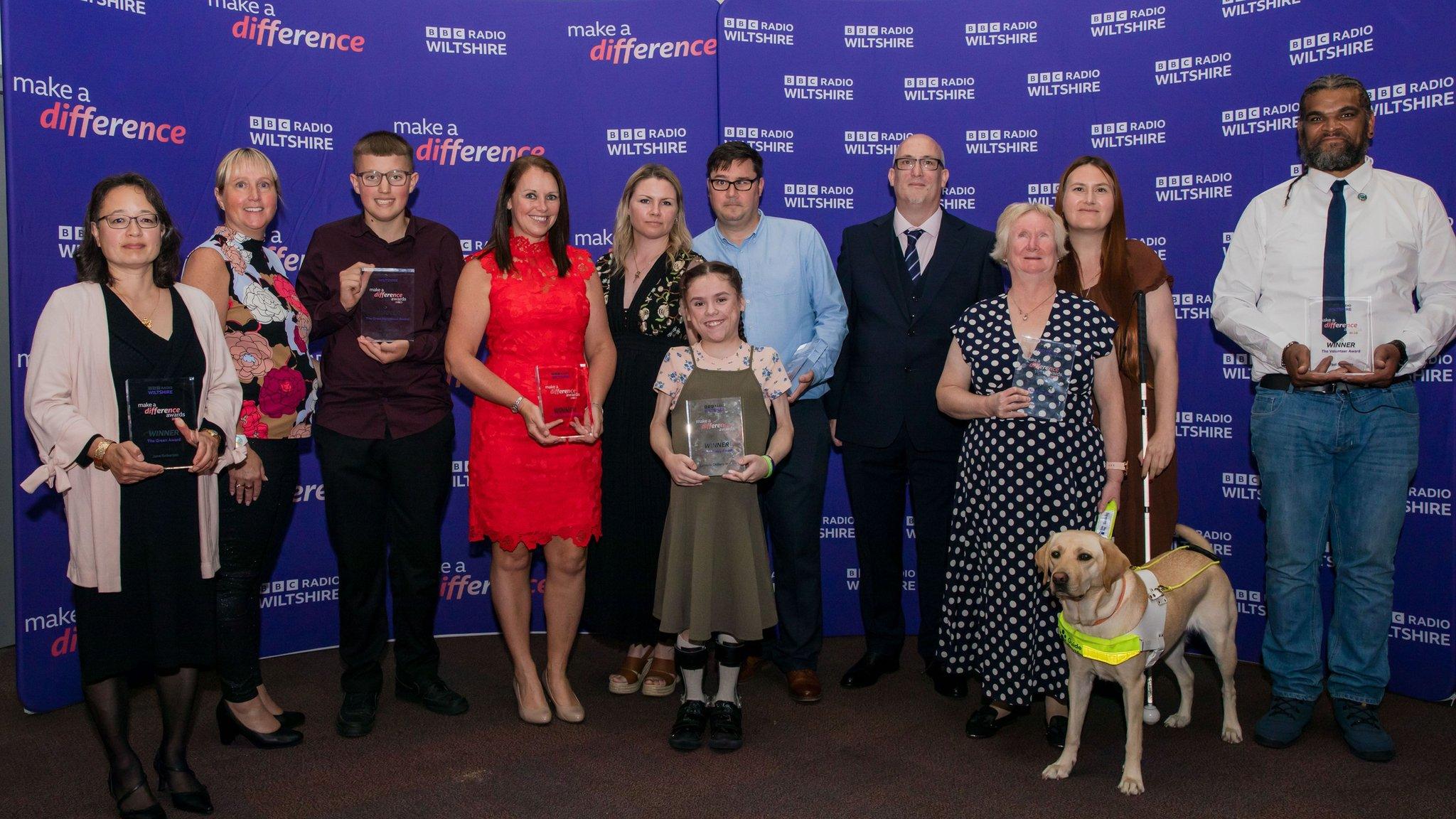 People in front of branded banner holding glass awards.