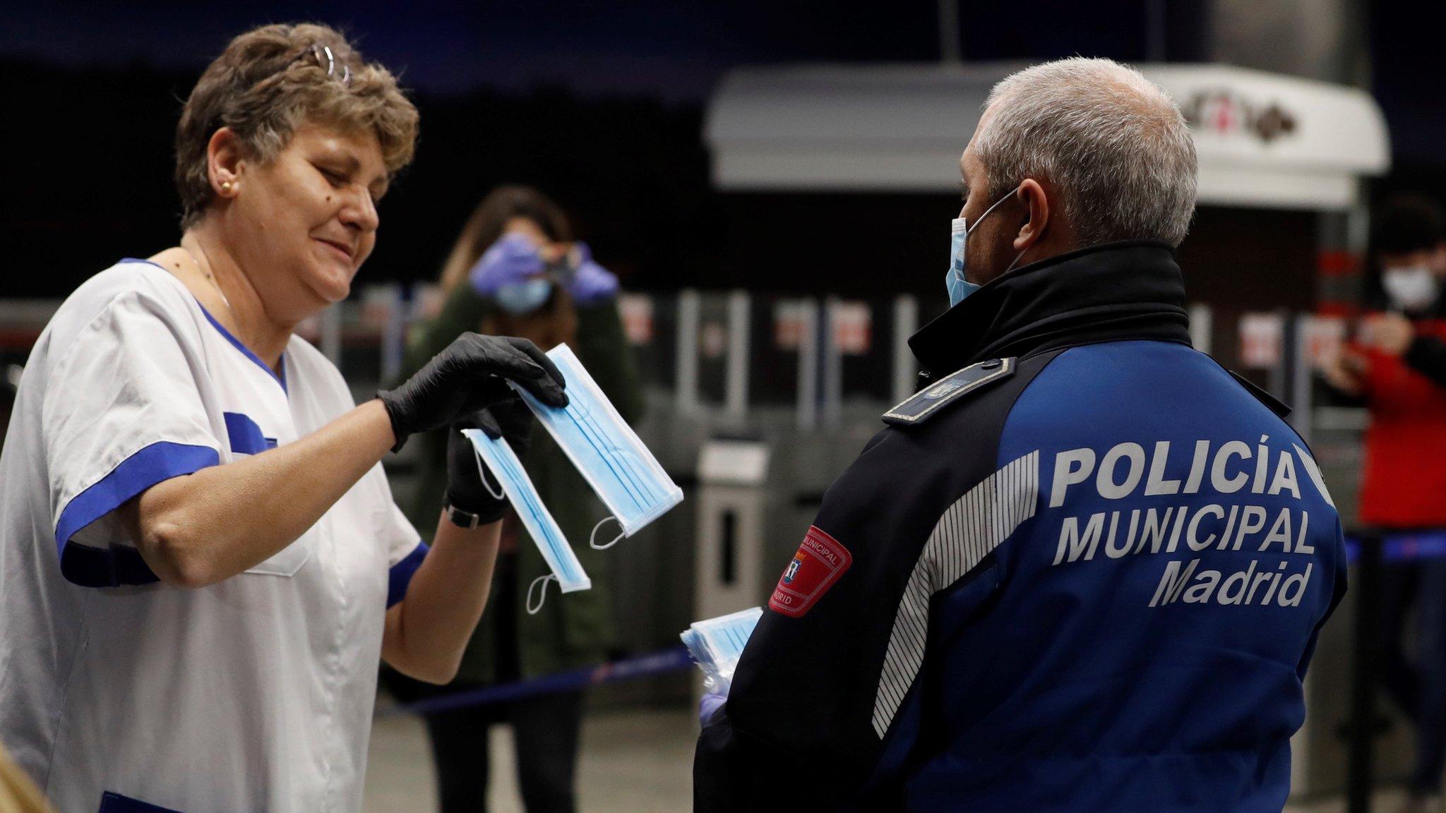 A policeman hands a mask to a commuter at Nuevos Ministerios metro station in Madrid, Spain (13 April 2020)