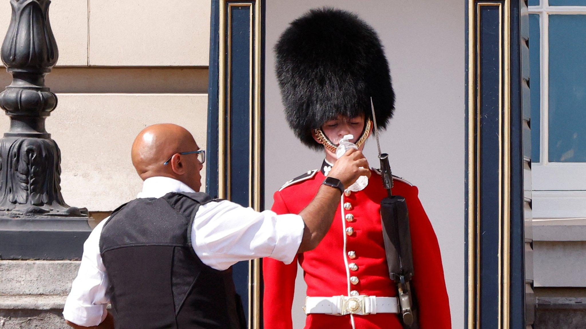 a queen's guard at their station drinks from a bottle of water provided by a member of security