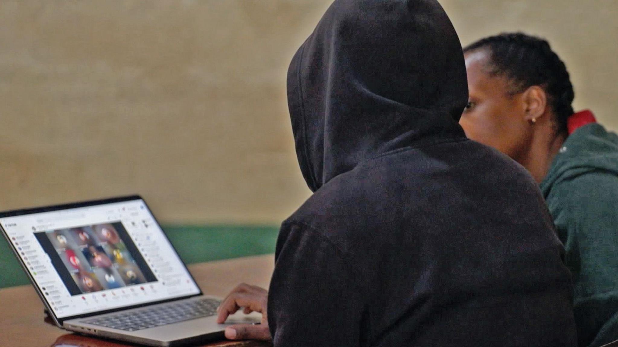 A moderator, shown from behind and in a dark hoodie to anonymise them, shows the BBC reporter a laptop showing blurred out images from TikTok