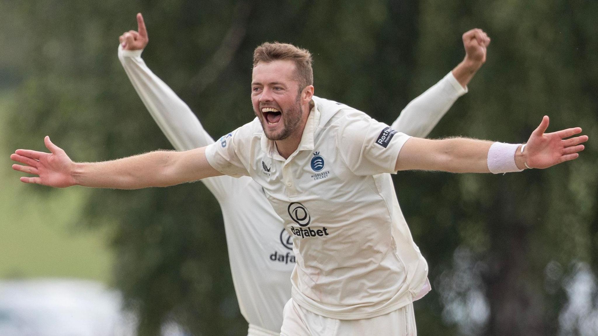 Tom Helm stretches out both arms in celebration after taking a wicket for Middlesex