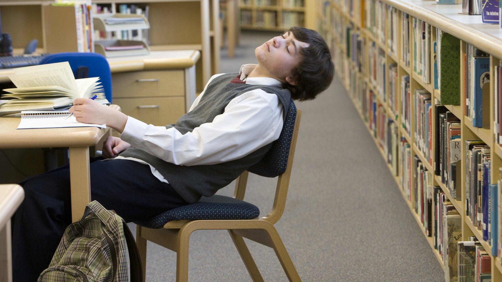 Teenager asleep at desk in school library