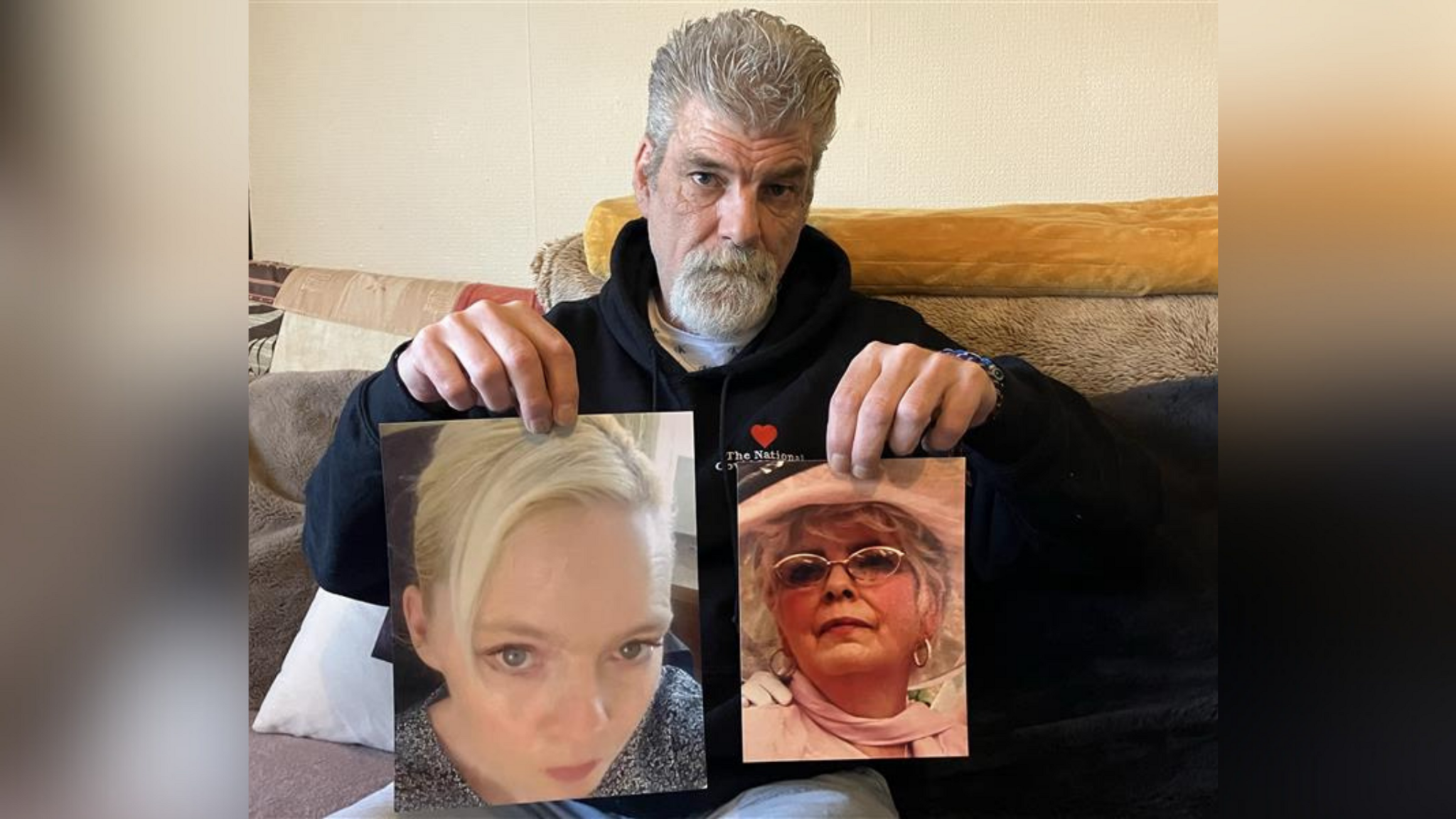 Charles Persinger looks at the camera while holding up large photographs of his wife and his mother who both passed away during the Covid pandemic