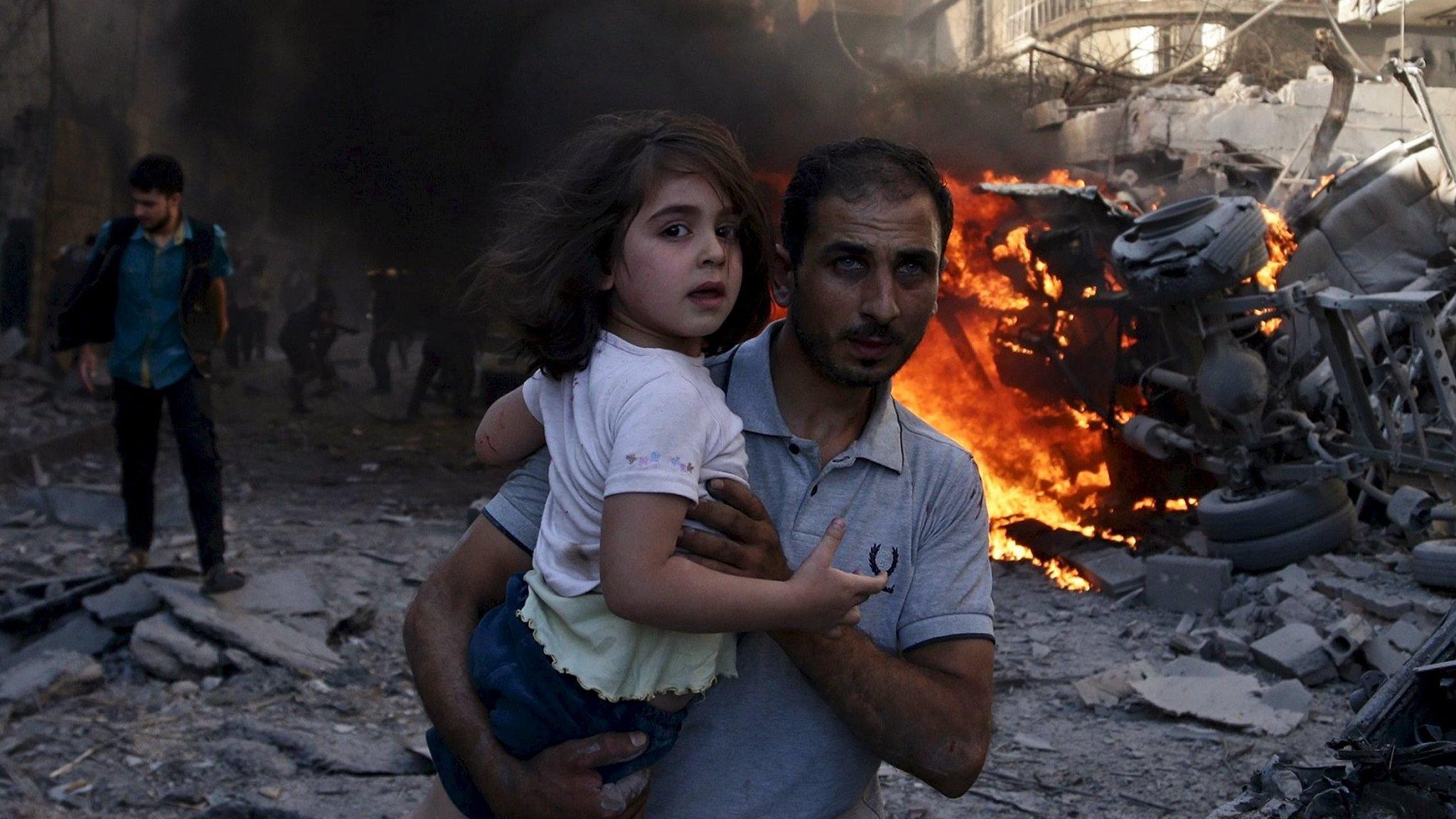 A man carries a girl as they run away from a site hit by what activists said were air strikes by forces loyal to Syria's President Bashar al-Assad in the Douma area of Damascus (24 August 2015)