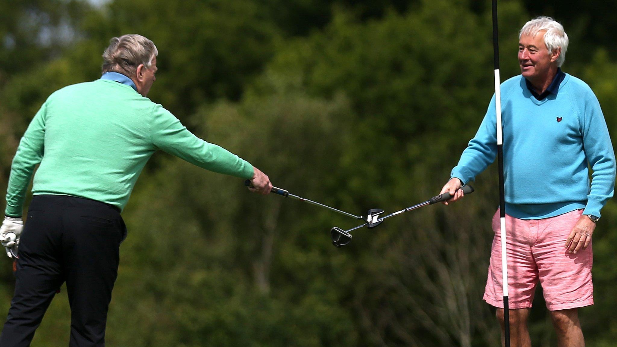 Two members touch clubs at the end of their round as a substitute for shaking hands at West Essex Golf Course