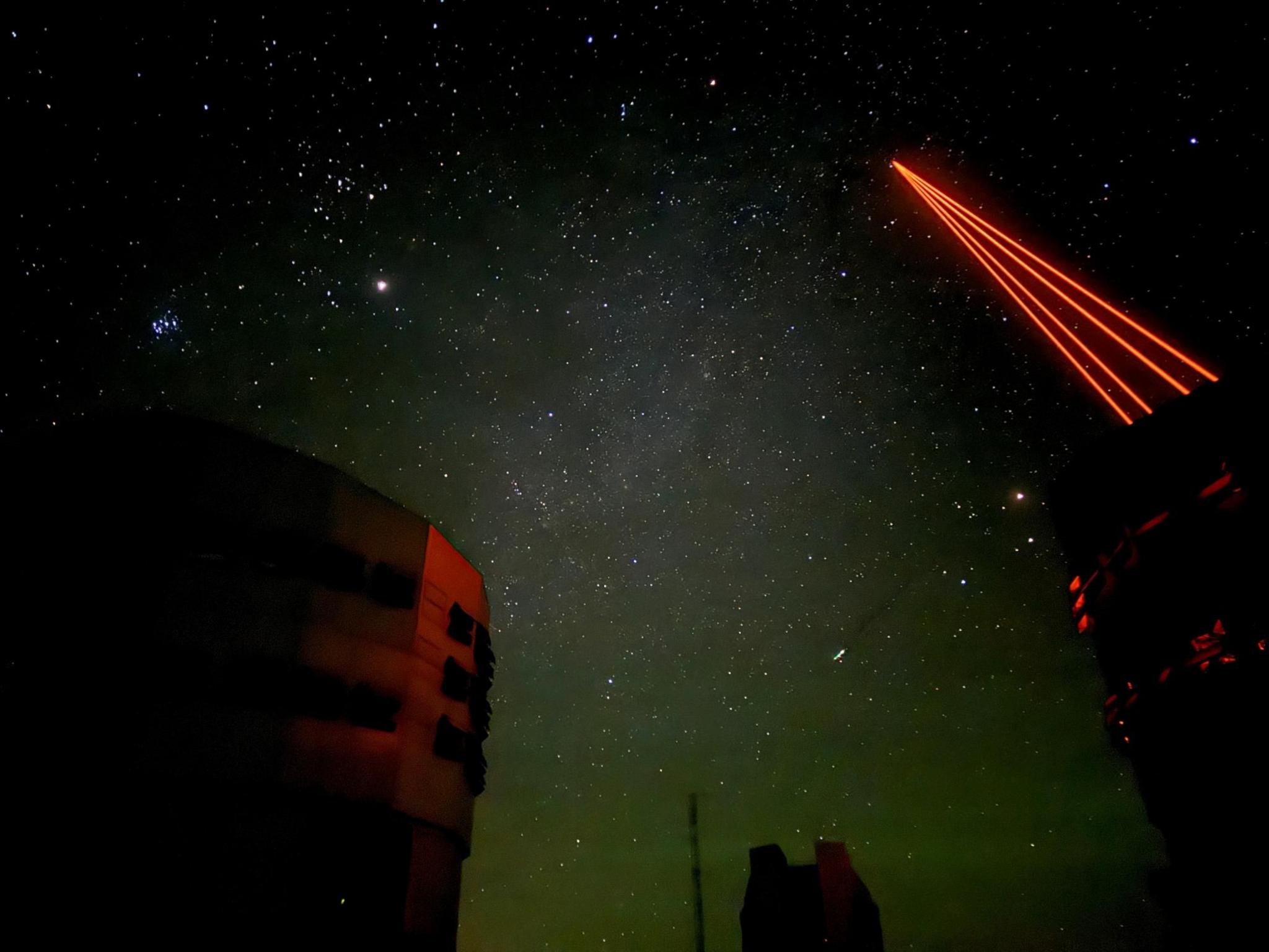 Red laser beams are sent into the night sky from the Very Large Telescope (VLT) at Paranal Observatory in the Atacama Desert. The night sky is filled with stars.