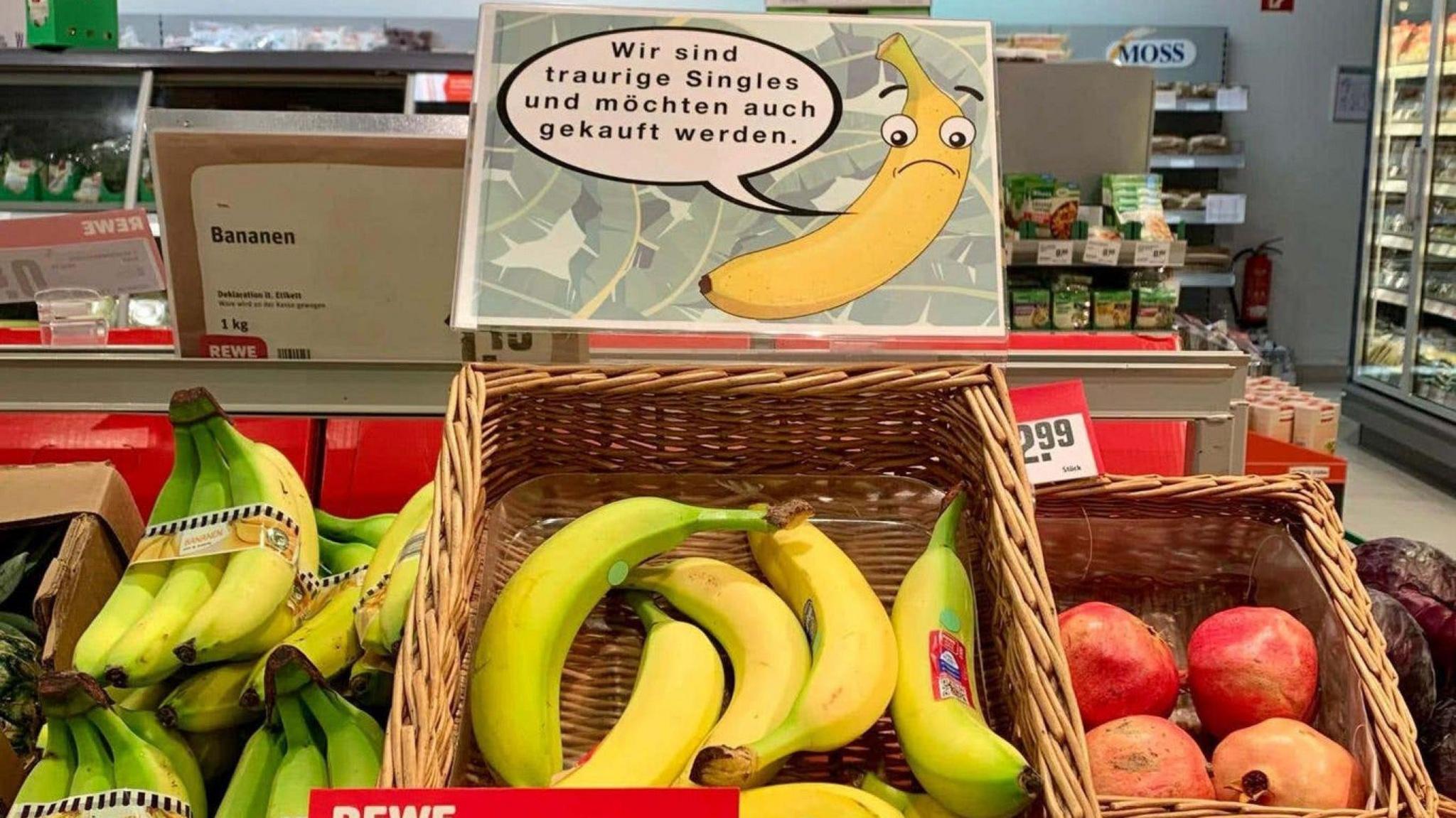 Single bananas are in a basket in a german supermarket. They have a sign showing a sad banana with a speech bubble with german in it. 