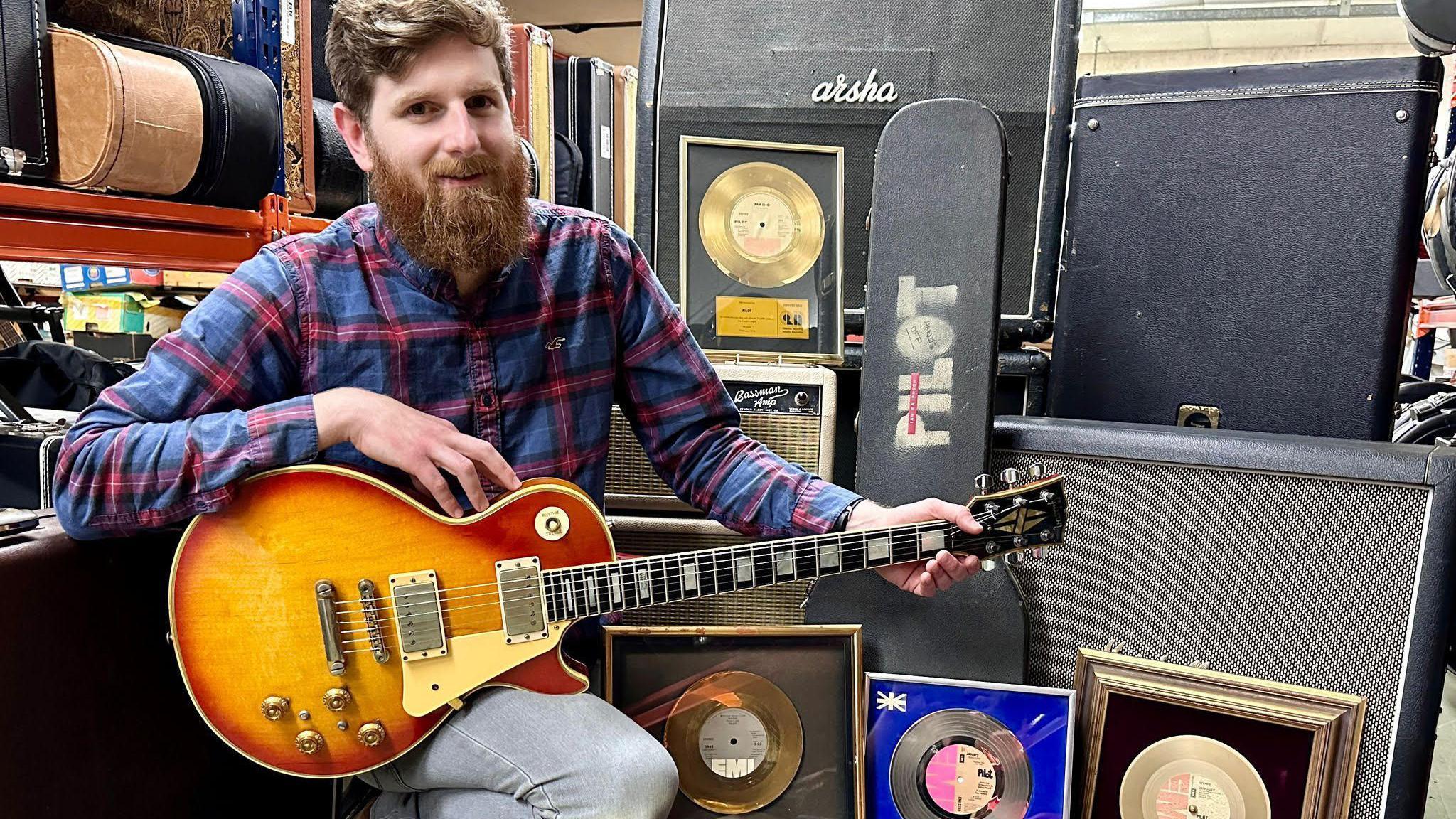 Auctioneer Luke Hobbs hllding Ian Bairnson's guitar and kneeling near the rest of the equipment