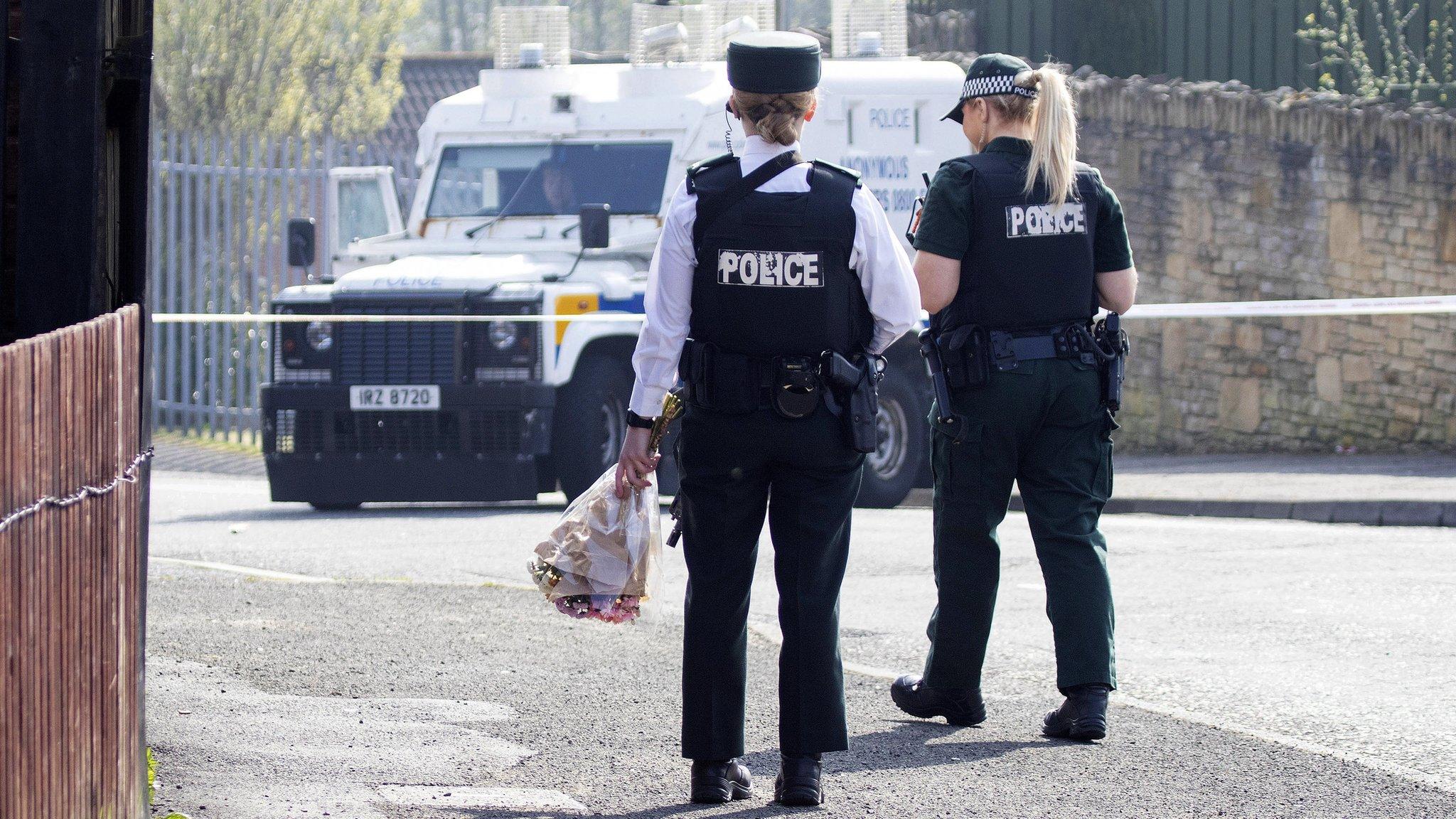 A police officer carries flowers to the area where Lyra McKee