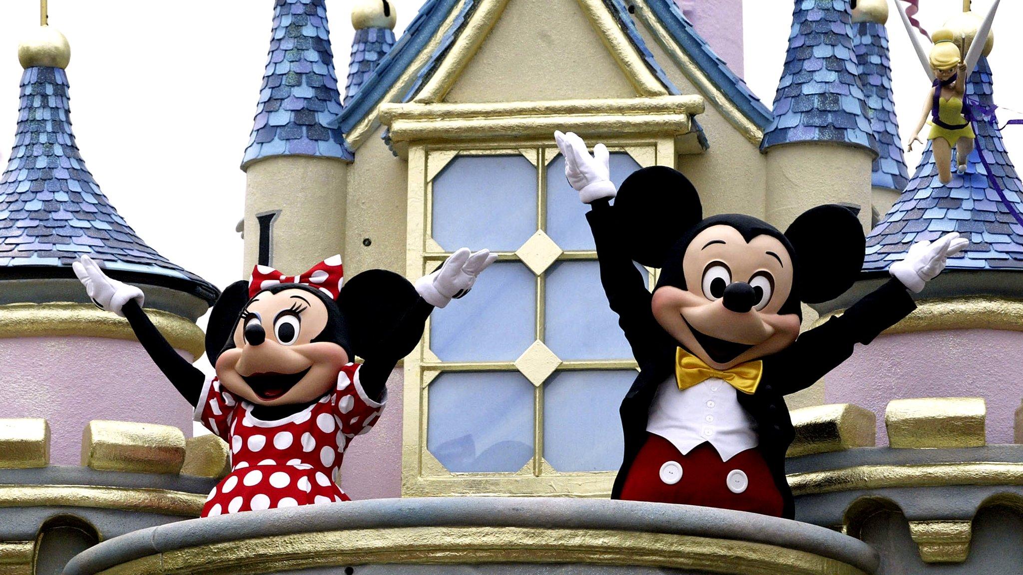 Mickey Mouse and Minnie Mouse stand on a balcony of a fantasy castle