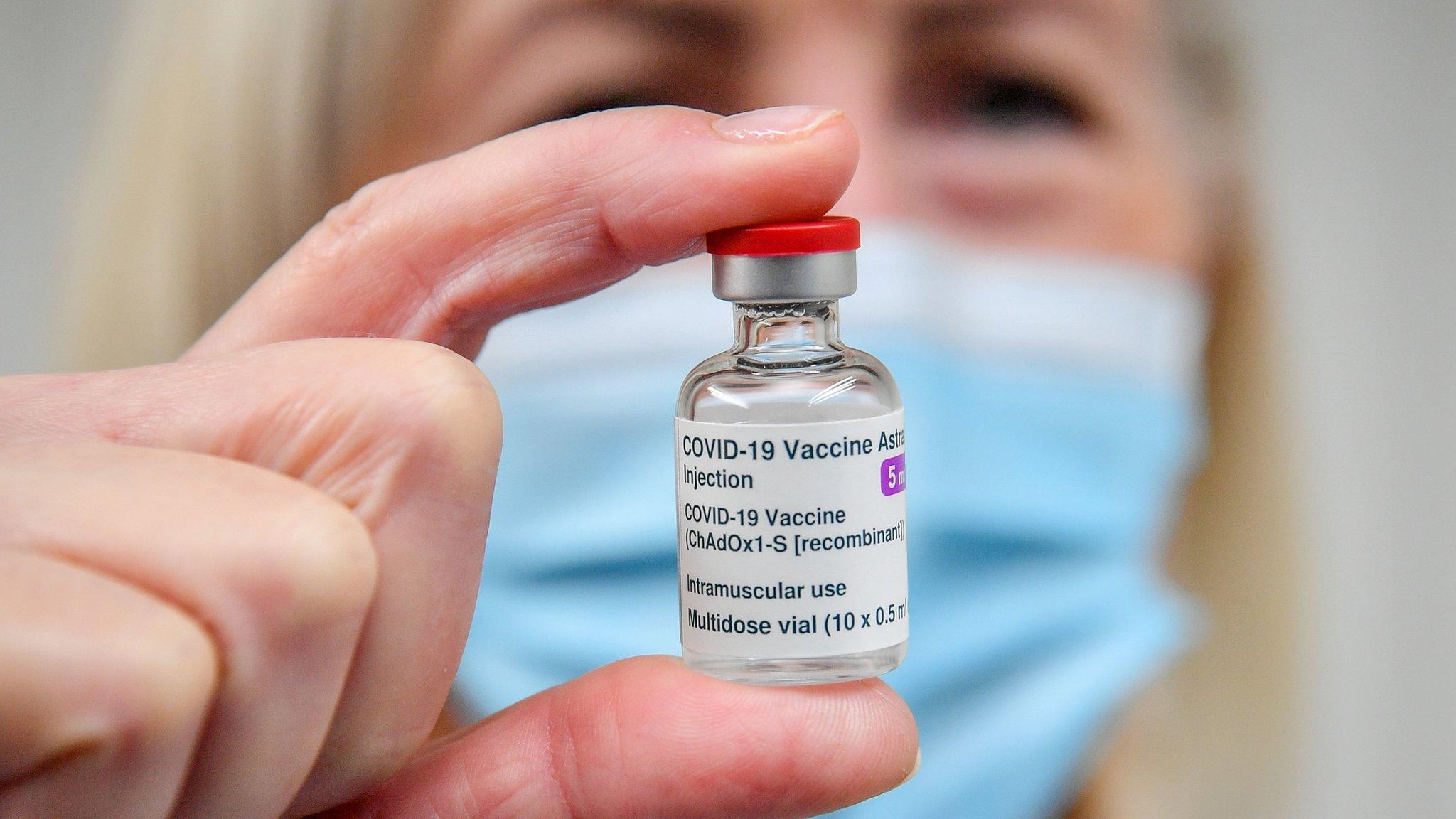 Person in facemask holding a Covid vaccine bottle