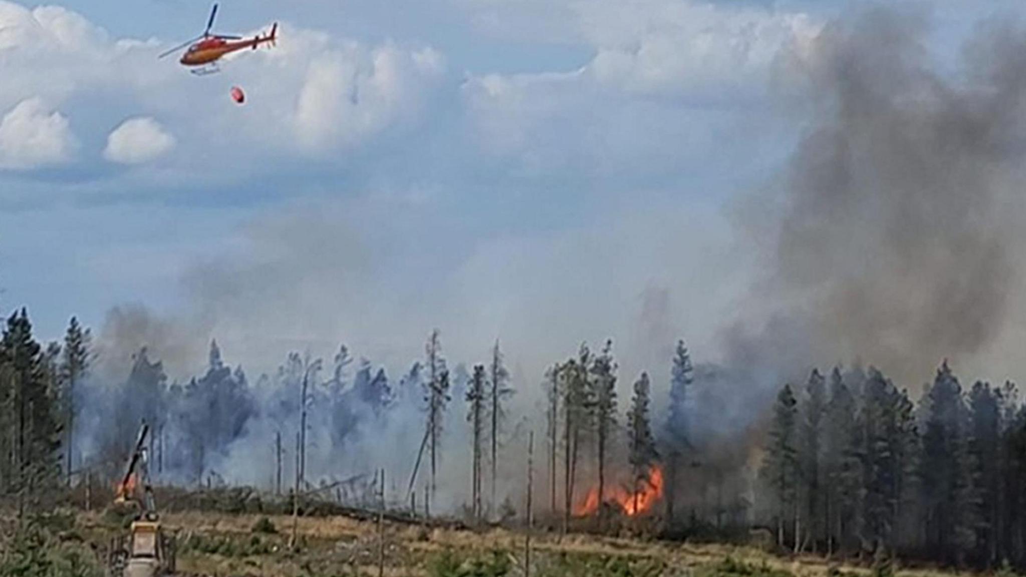 Image shows a large moorland fire on Langdale Moor in North Yorkshire with a helicopter seen at the top of the image carrying a large water bowser