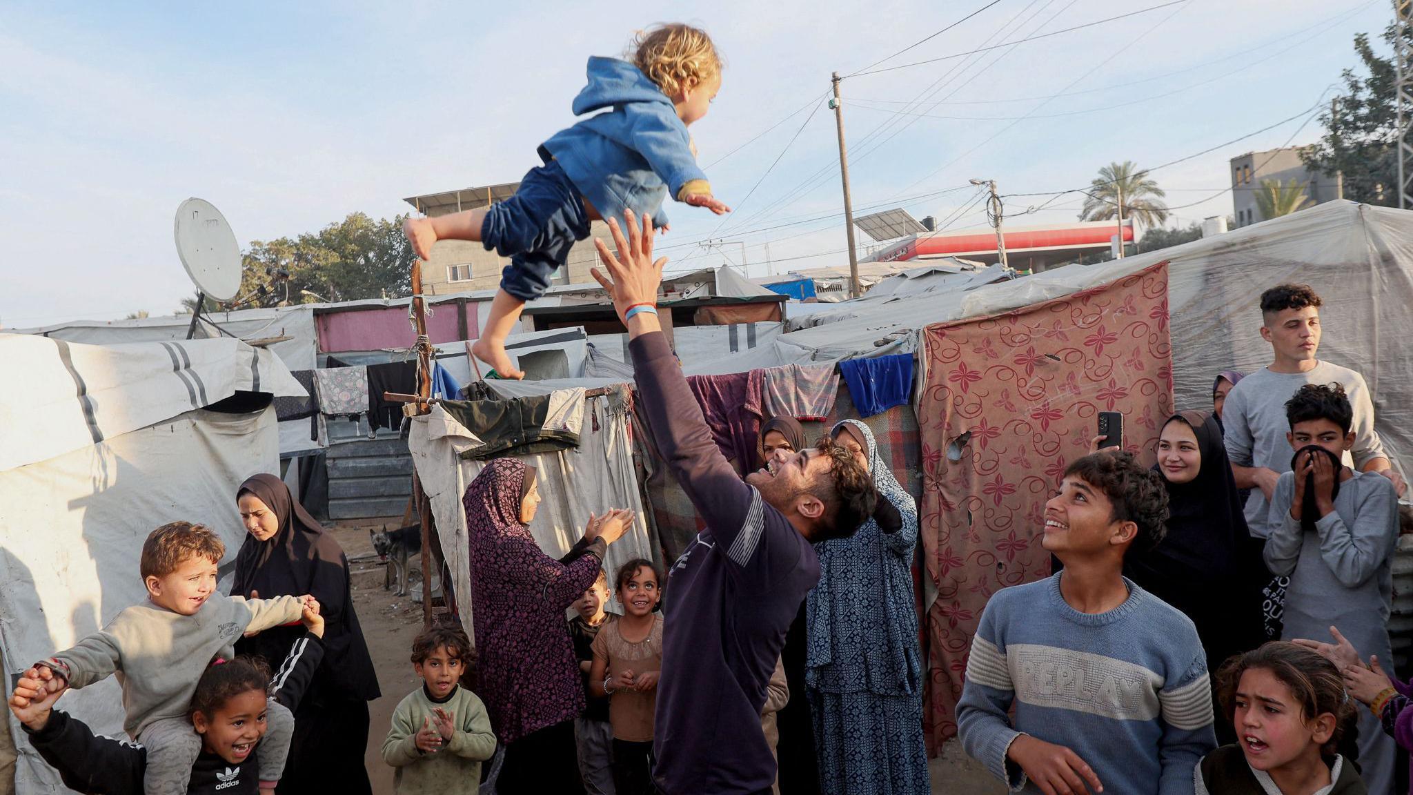 A man throws a child into the air at a camp in central Gaza for displaced Palestinians, following the beginning of the ceasefire on Sunday