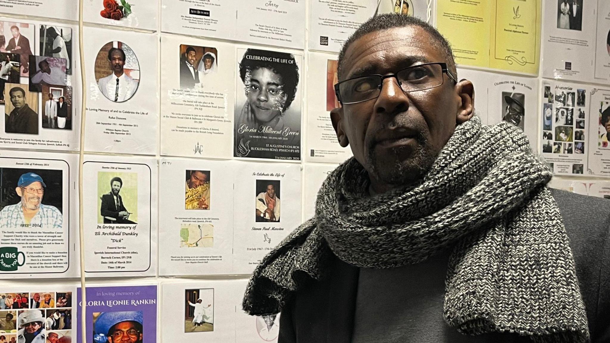 Max Thomas, who is wearing glasses and a scarf, stands in front of a display board inside an exhibition room