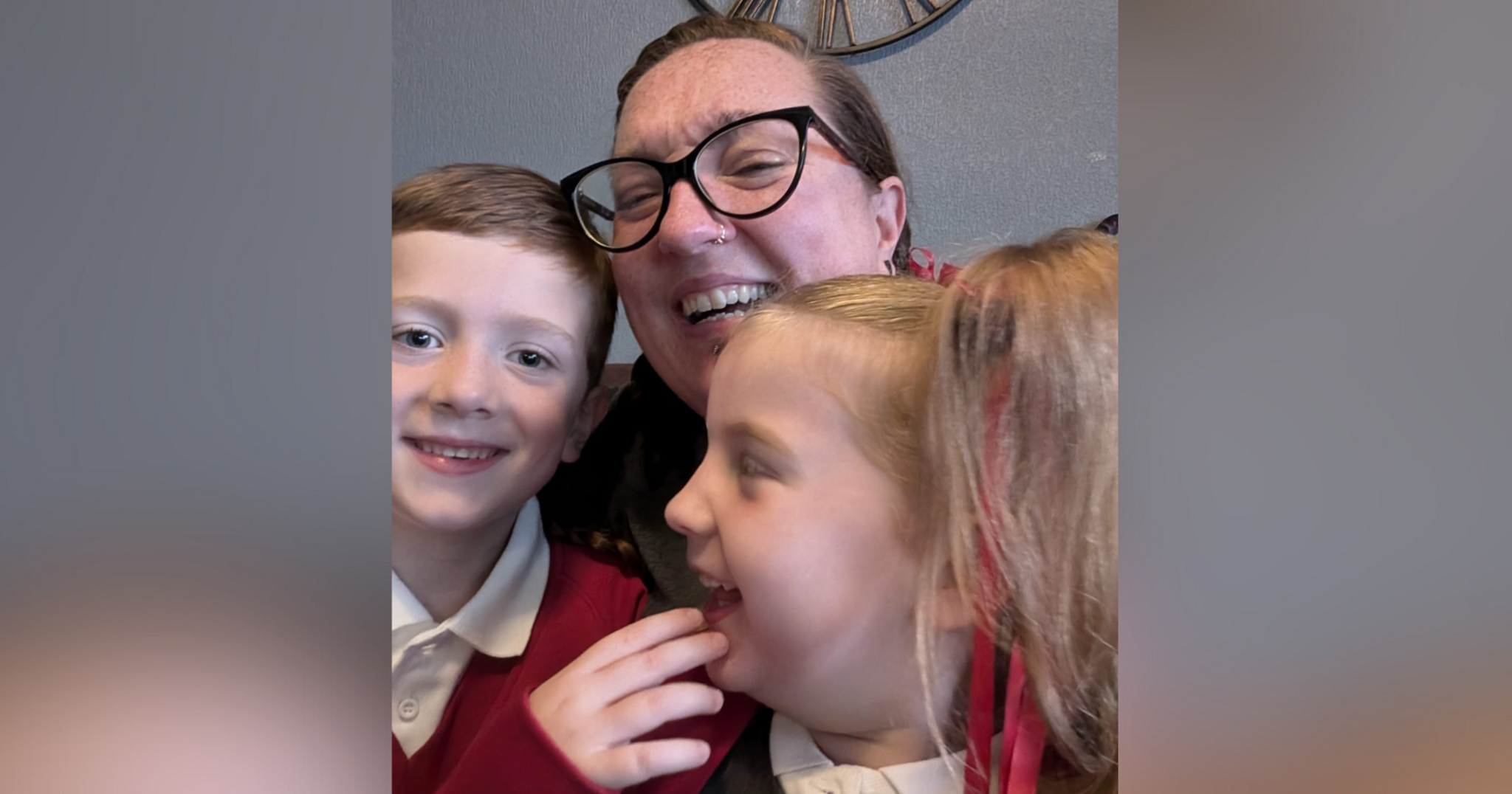 Debbie McCrudden, a woman with dark hair, a nose ring and black-framed glasses, holding her two children on her lap. Everyone in the photo is laughing.