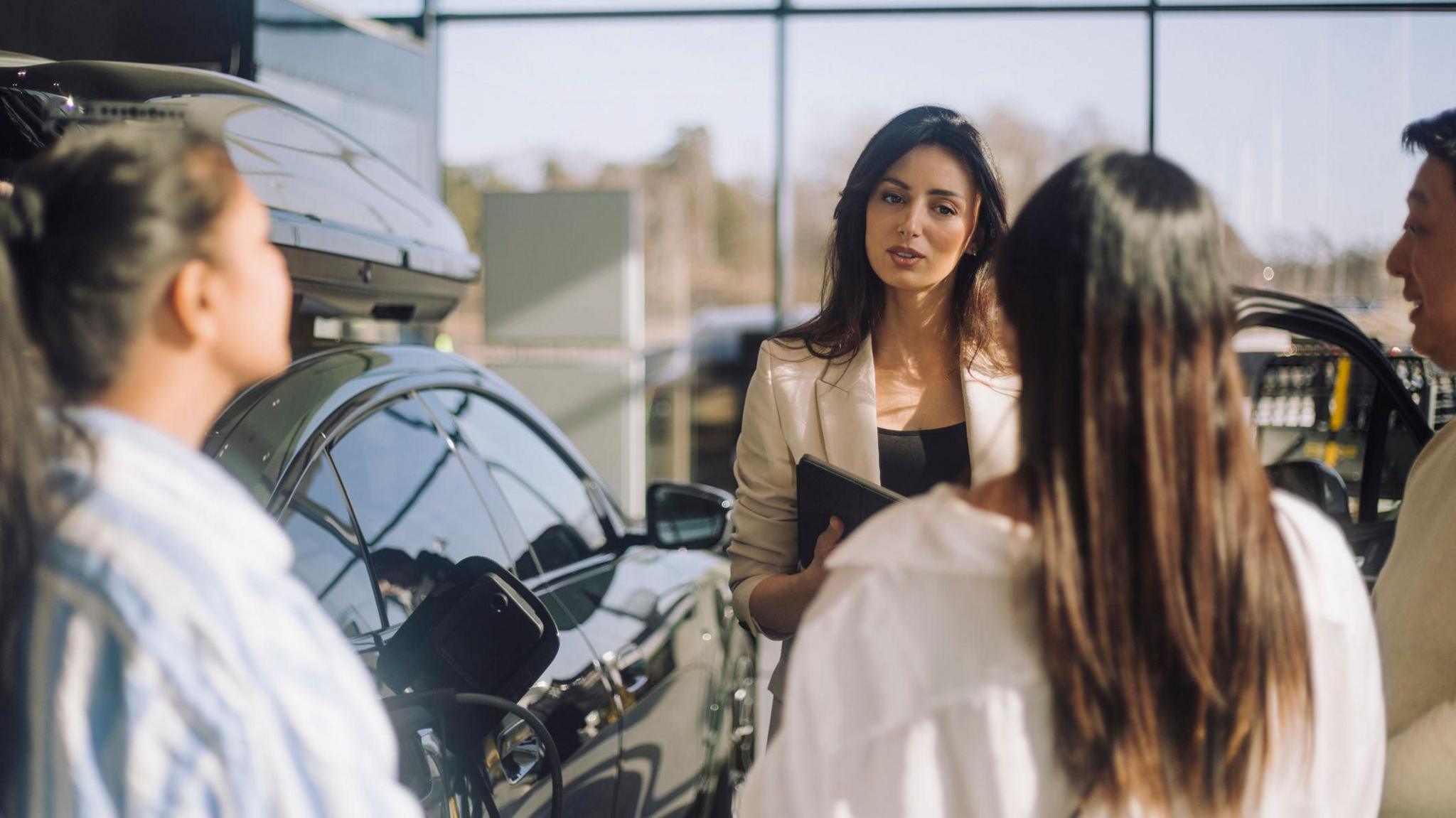 Female salesperson talking to customers in car showroom