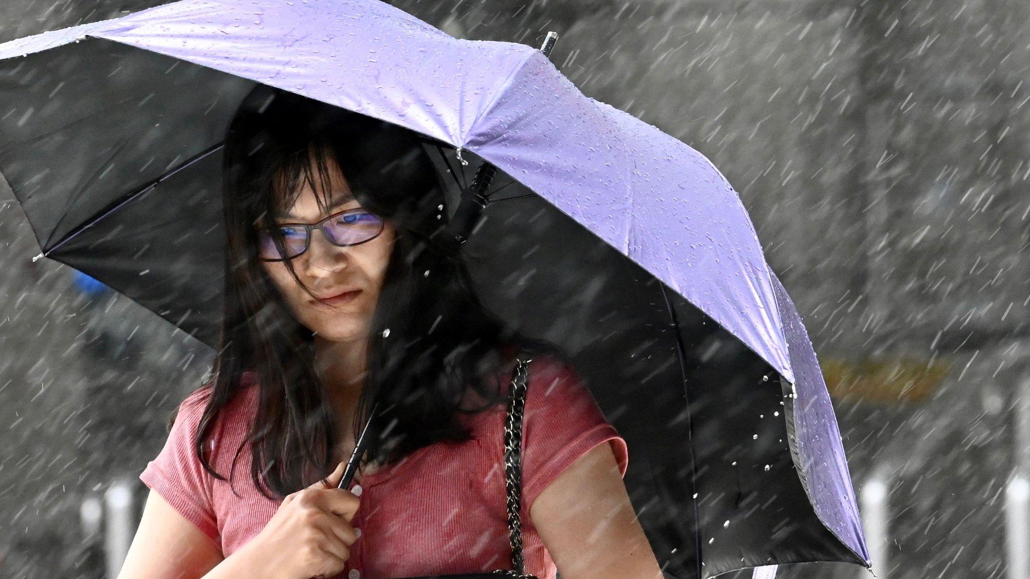 A woman shields herself with an umbrella as she walks in New Taipei City in rain brought by Typhoon Lekima as it passes northeastern Taiwan on August 9, 2019