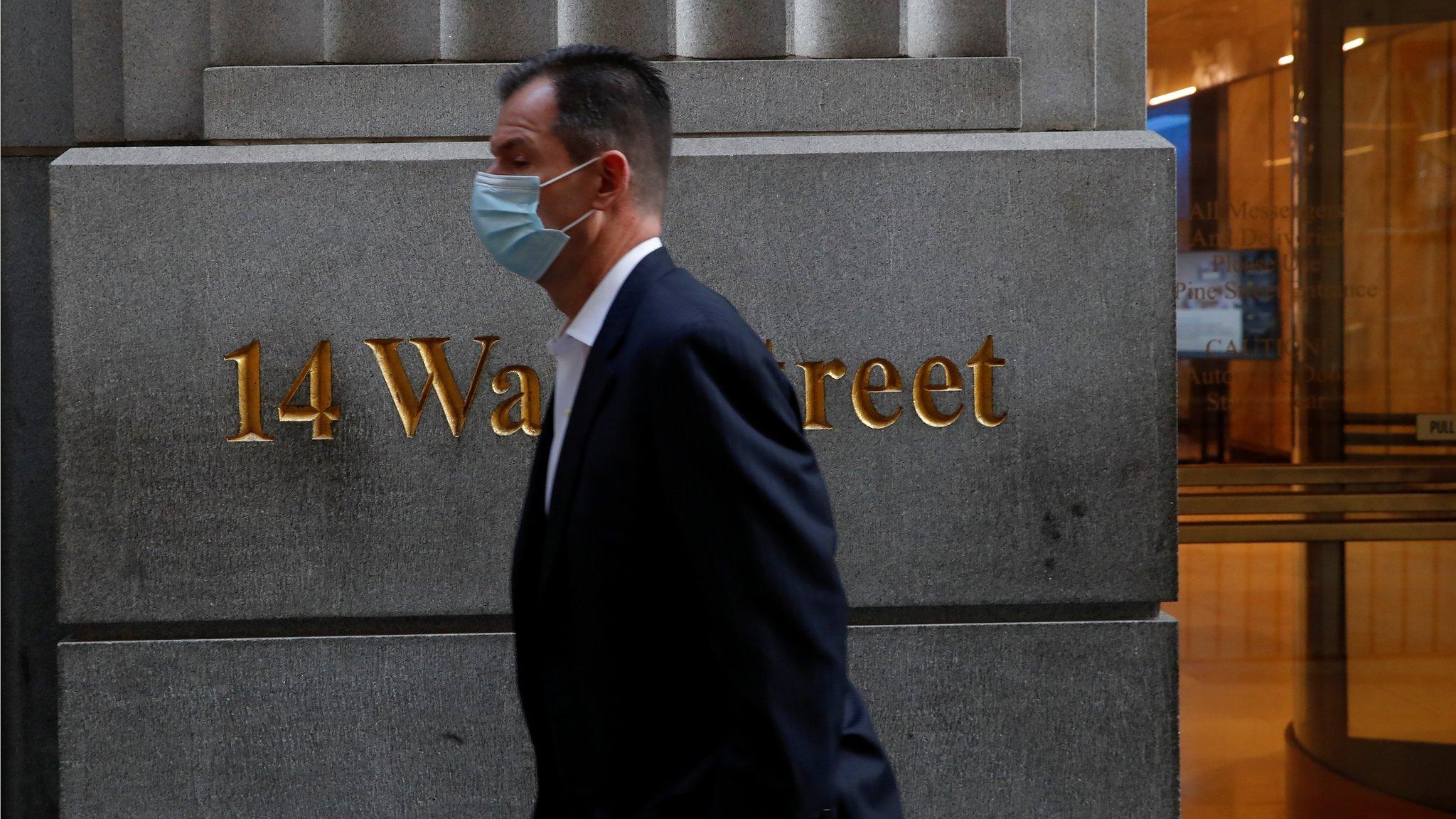 man wearing a protective face mask walks by 14 Wall Street, as the global outbreak of the coronavirus disease (COVID-19) continues, in the financial district of New York, U.S., November 19, 2020