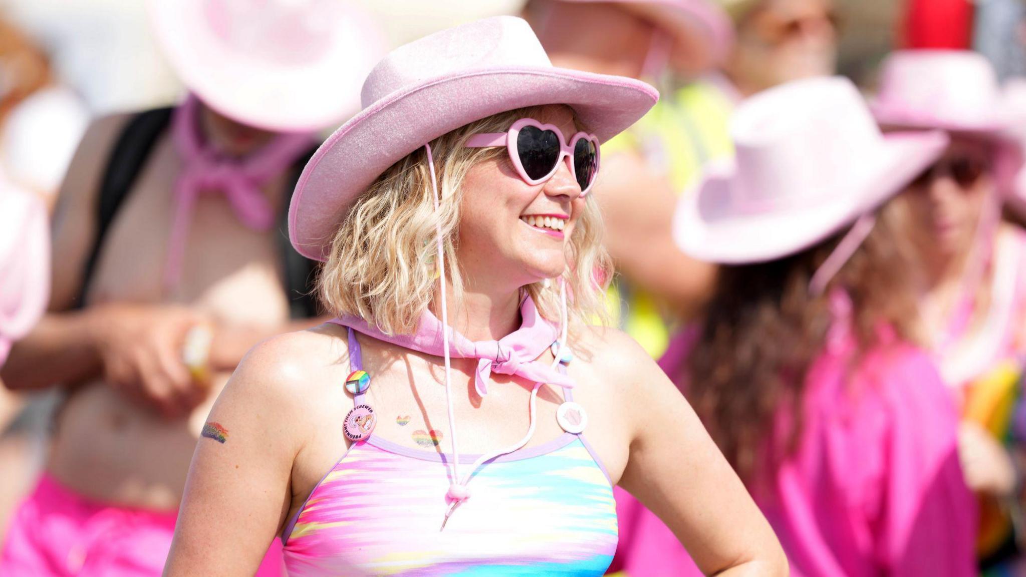 A woman wearing a bright pink bathing suit and hat, as well as pink heart-shaped sunglasses.