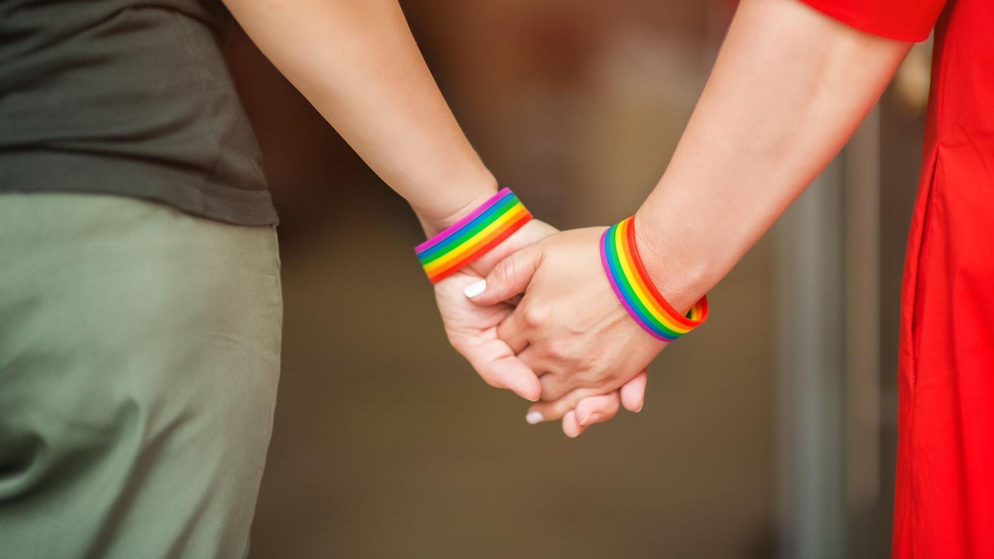 Close up of two people holding hands wearing rainbow wrist bands