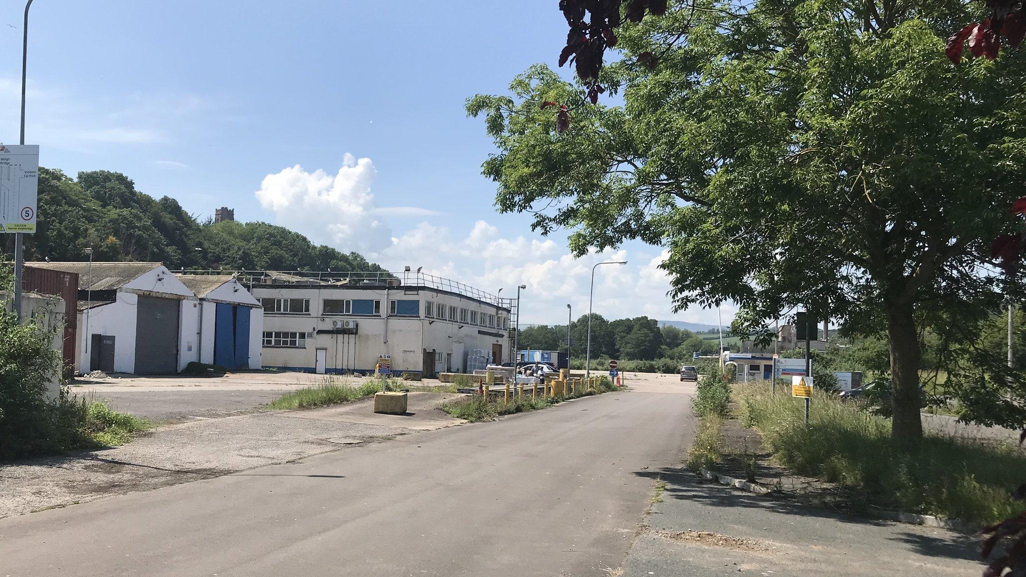 White industrial buildings with a service road running through and a tree on a sunny day