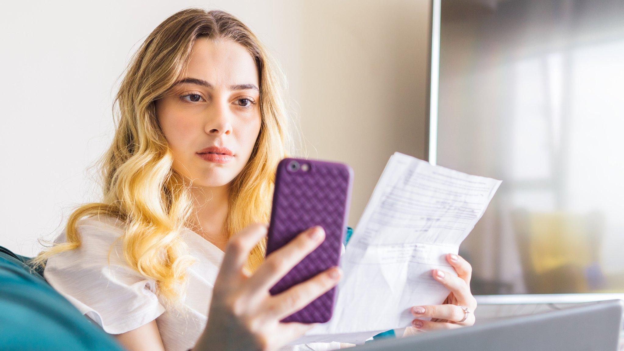 Woman looking at her phone and a piece of paper