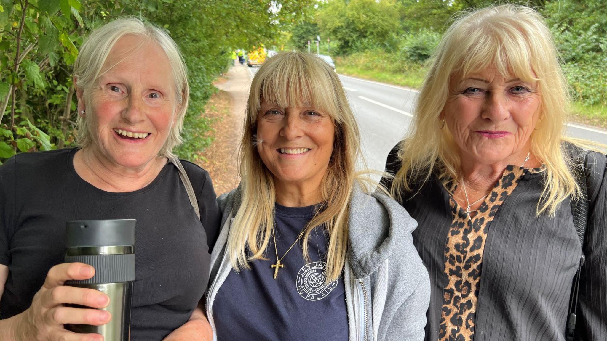 Three women standing in a row next to each other. They all have blonde hair and smiling at the camera.