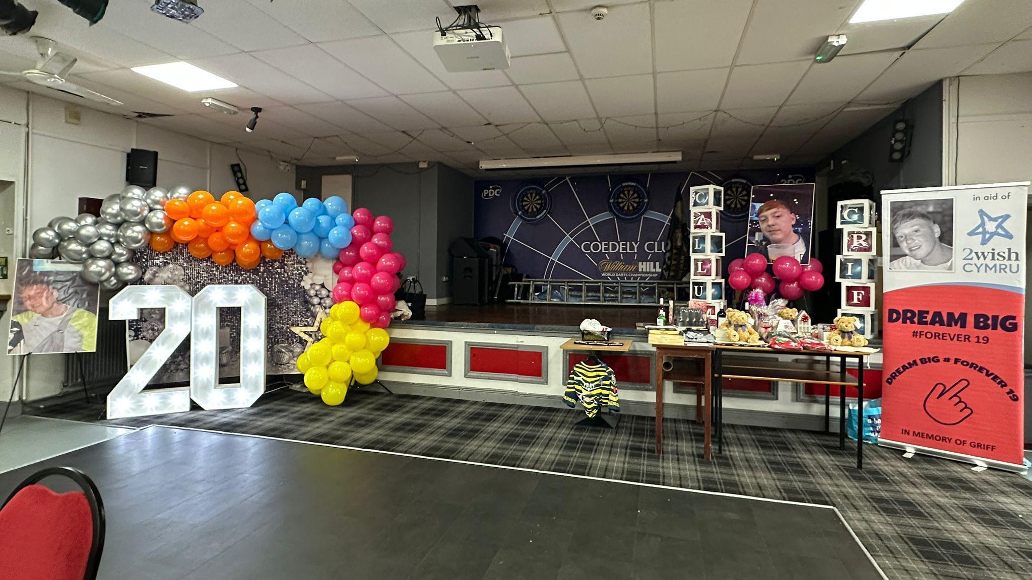 A light up 20 sign with balloons surrounding and pictures of Callum Griffiths in a room ahead of a party for his 20th birthday