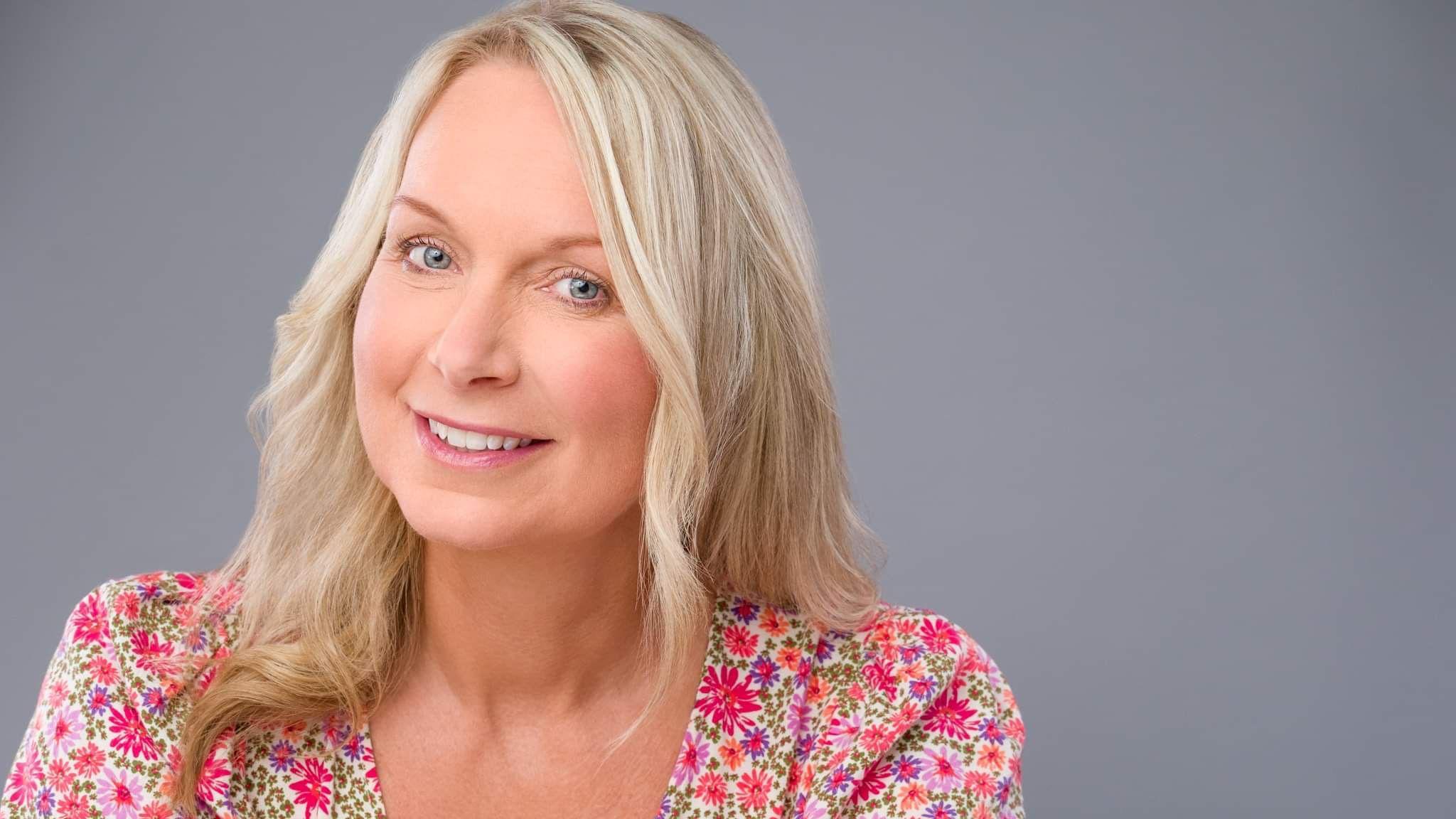 A woman with blonde hair and a flowery shirt smiling at the camera. 