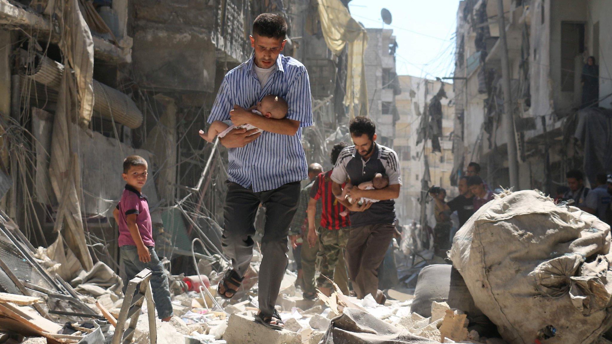 Men carry babies through the rubble of buildings destroyed in a reported government air strike in rebel-held Aleppo, Syria (11 September 2016)