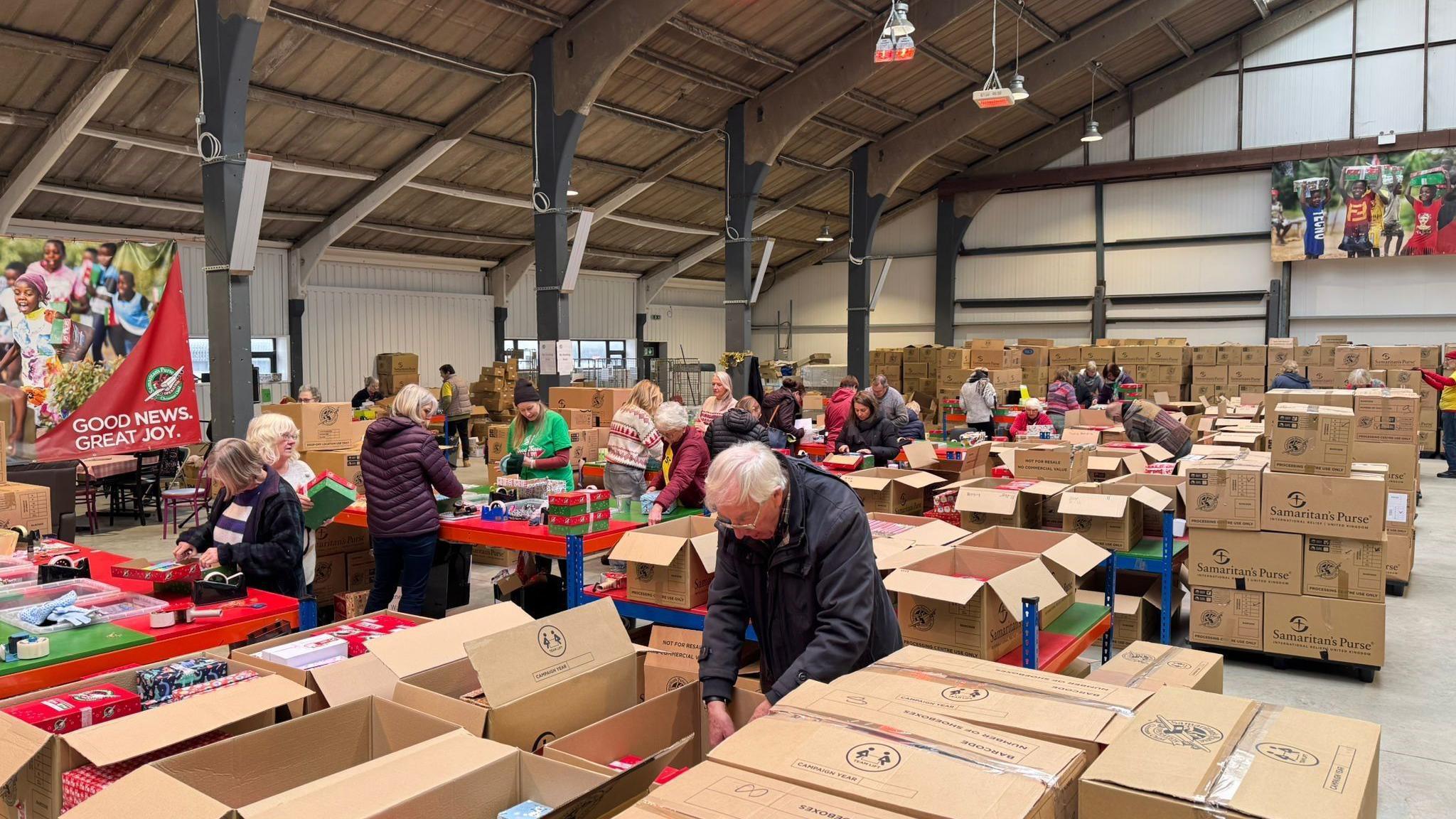 A sorting centre, there are lots of cardboard boxes and volunteers all taping boxes or checking them. 