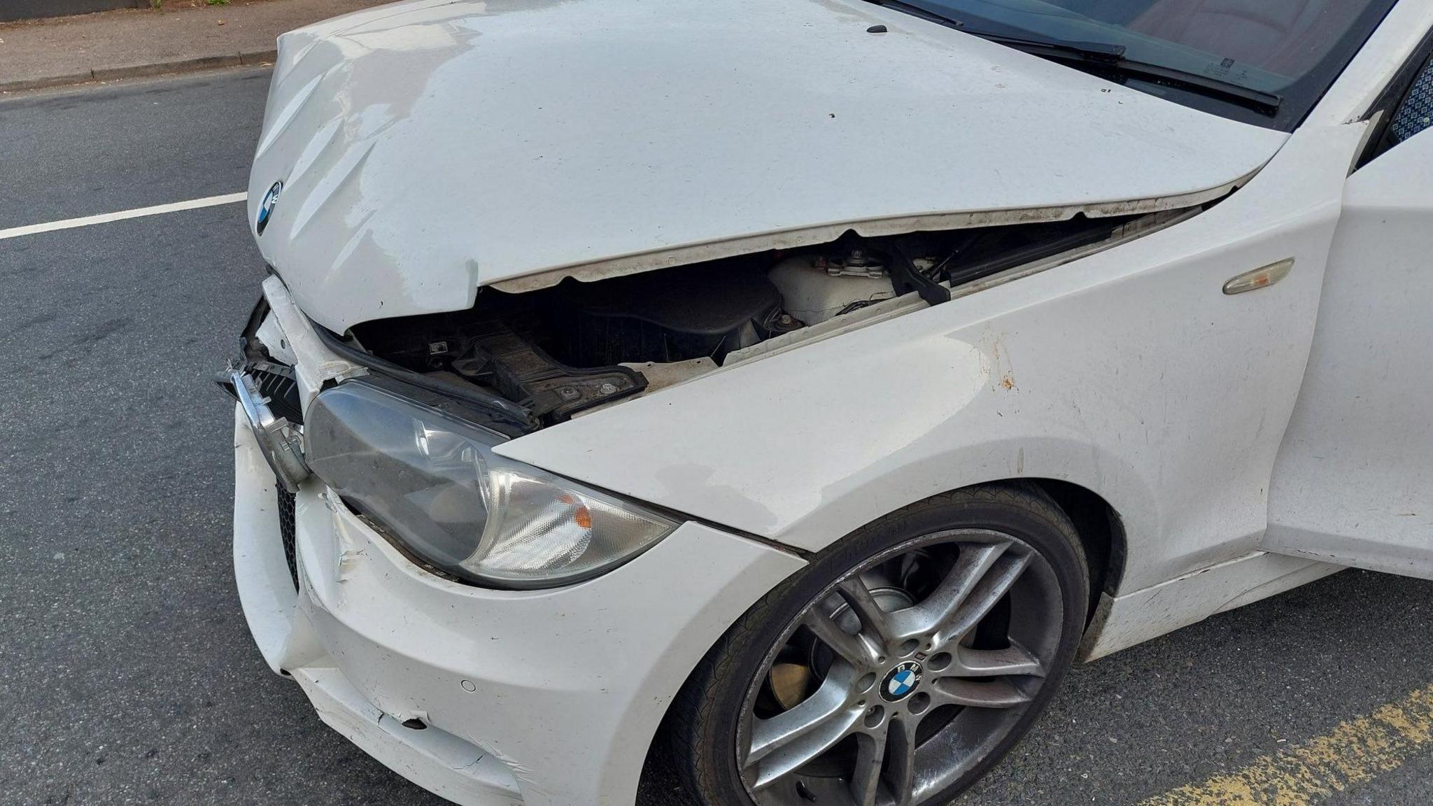 Part of the front passenger side of a white BMW car shows damage to the bonnet and the bumper