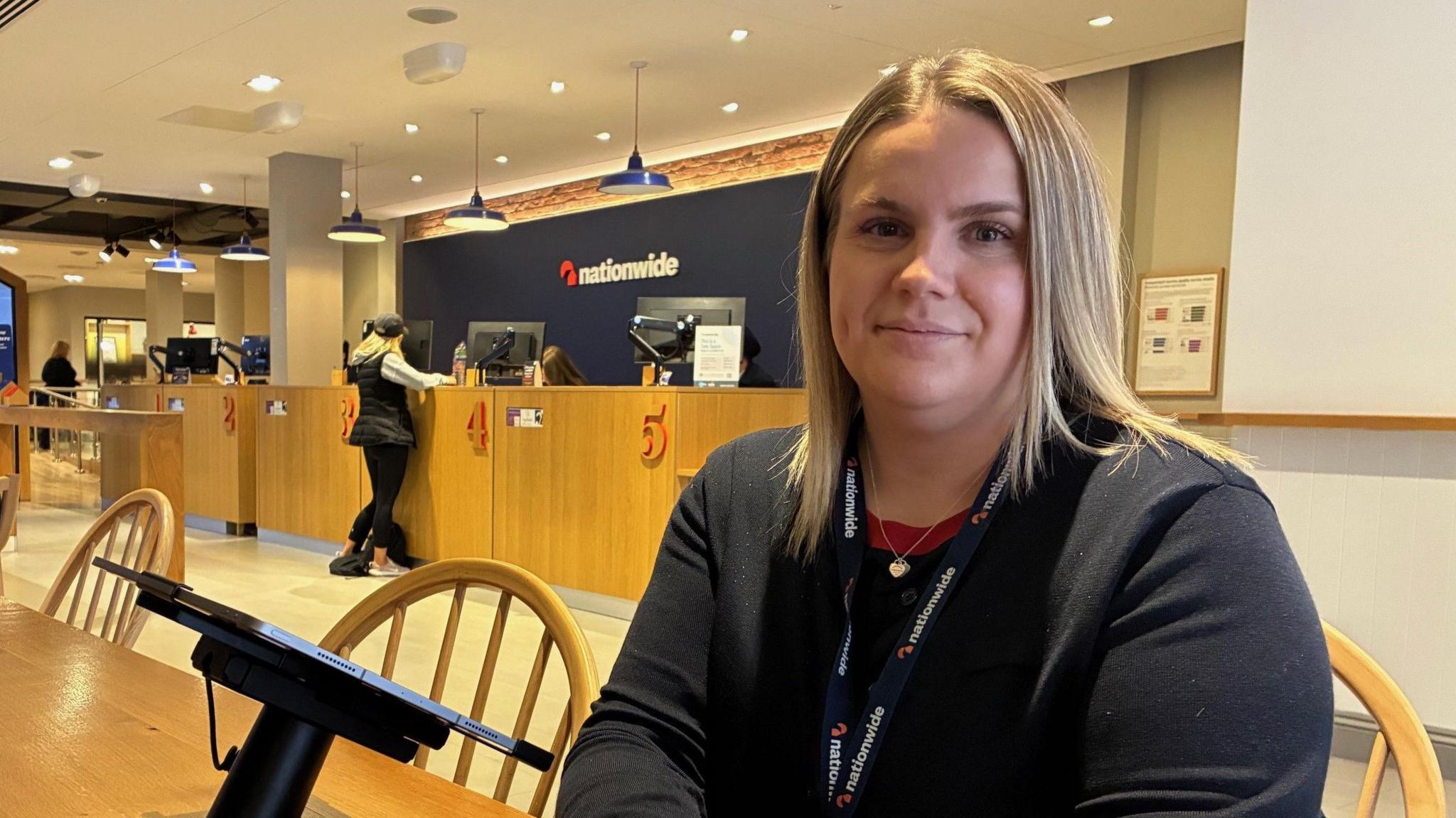 Jessica Bleasby, senior branch manager at Reading branch of Nationwide Building Society sits at a counter with the main customer counters of the branch behind her