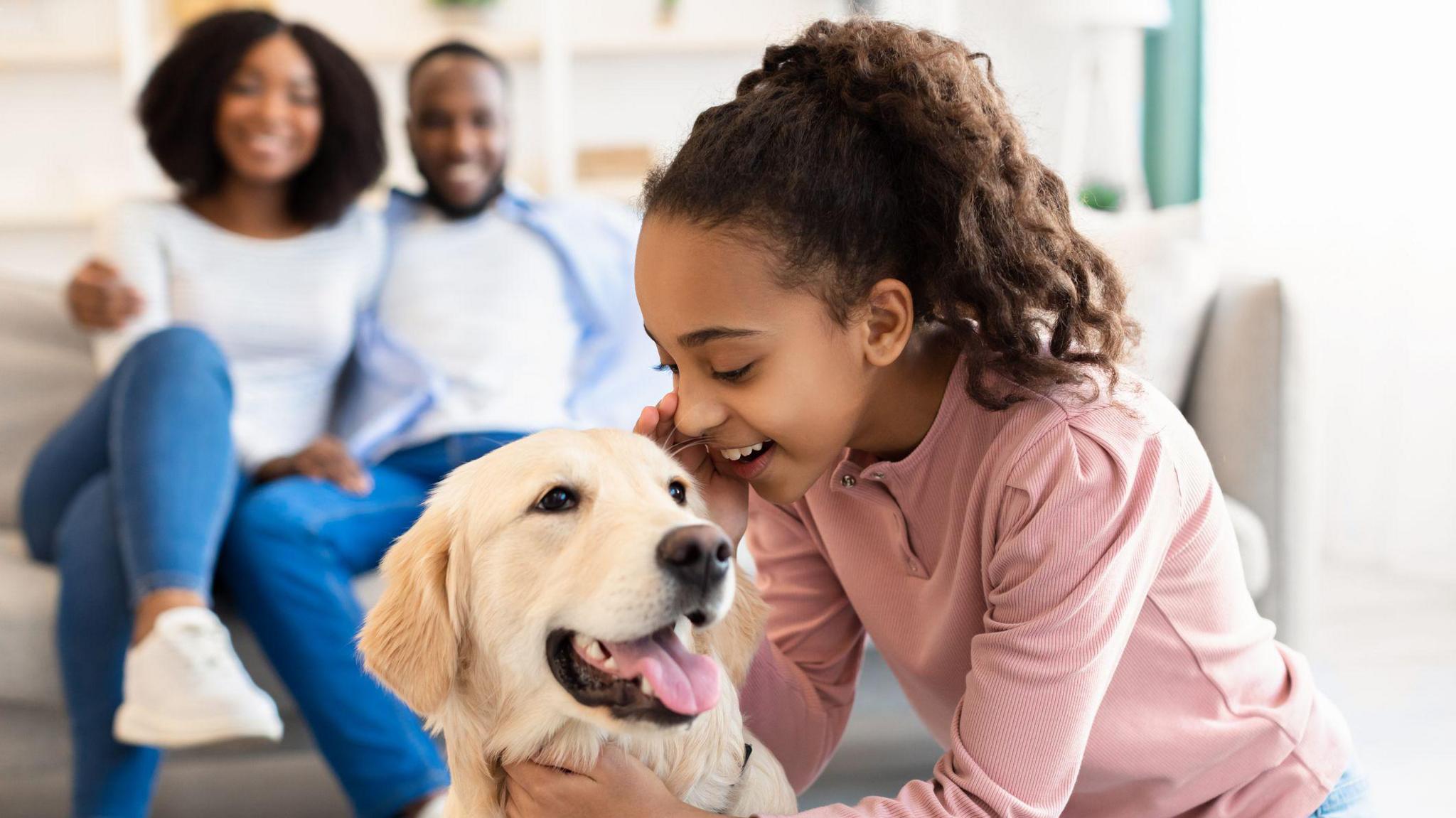 Girl whispering in dog's ear with parents sitting in the background.