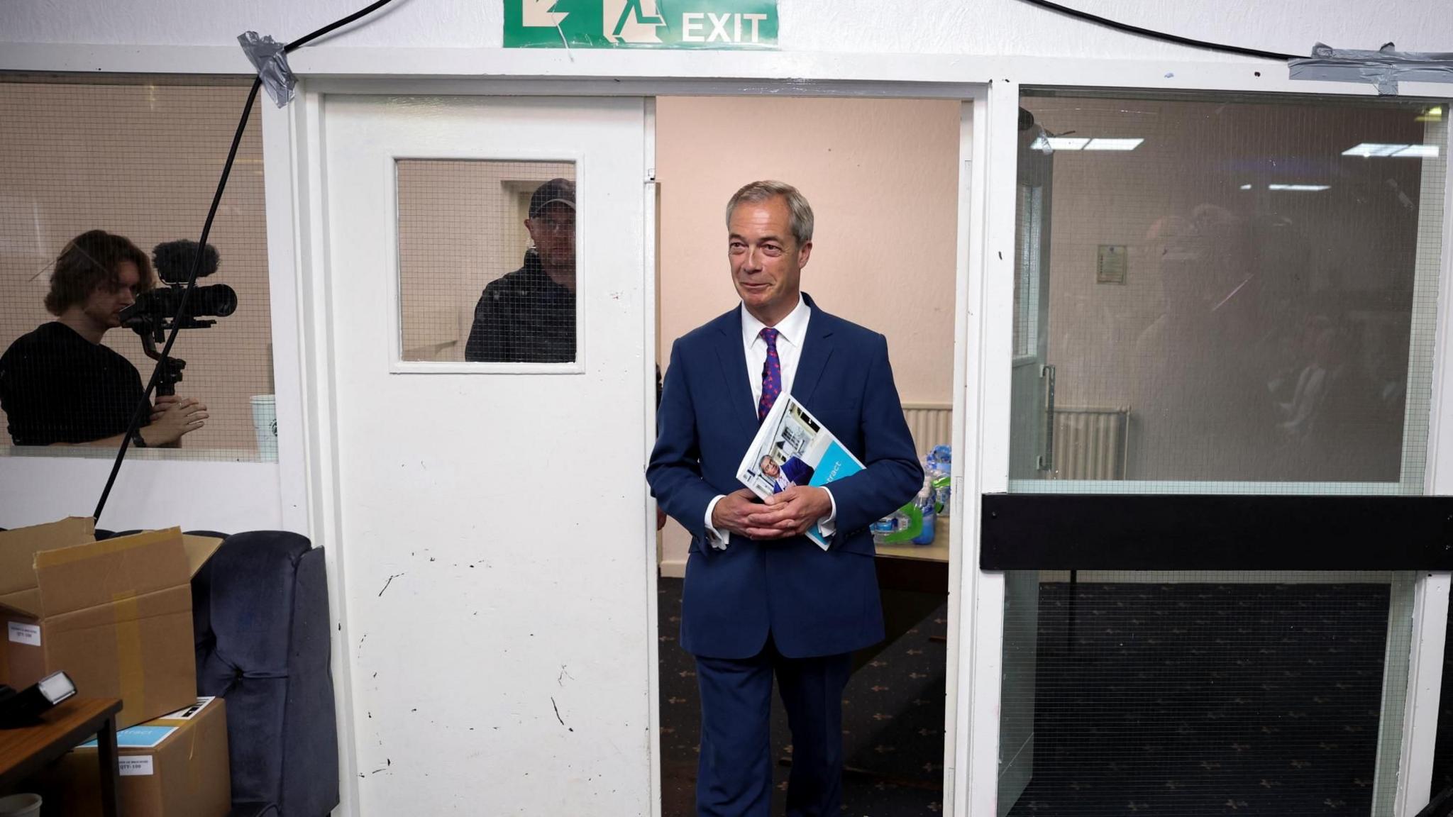 Nigel Farage walking through a door holding documents at the Gurnos social club  in Merthyr Tydfil at an event to launch Reform UK's manifesto