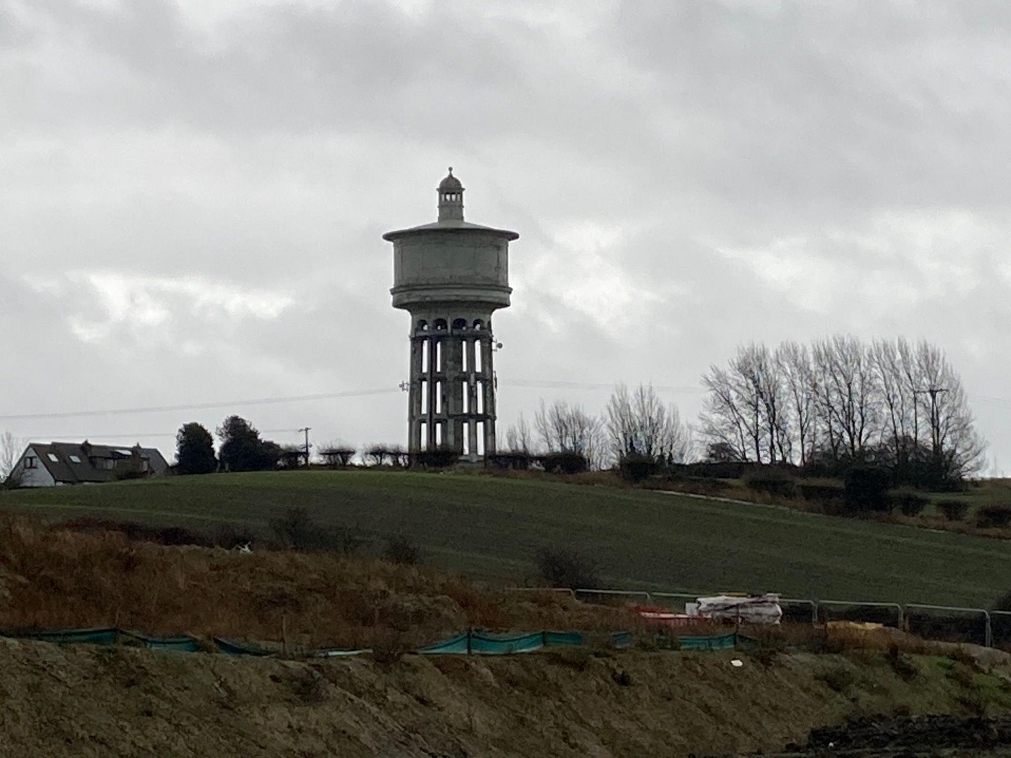 A concrete water tower in the distance surrounded by green fields and the roof of a house in the far left