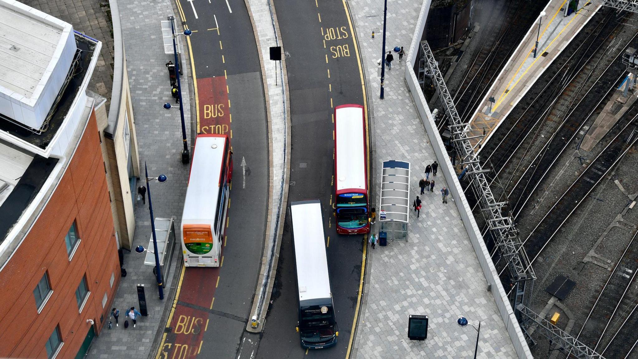 Aerial view of National Express West Midland buses, taken from the top of the Rotunda, Birmingham. There are three buses in the picture and you an see yellow bus stop road markings as well as small people on the ground below. 