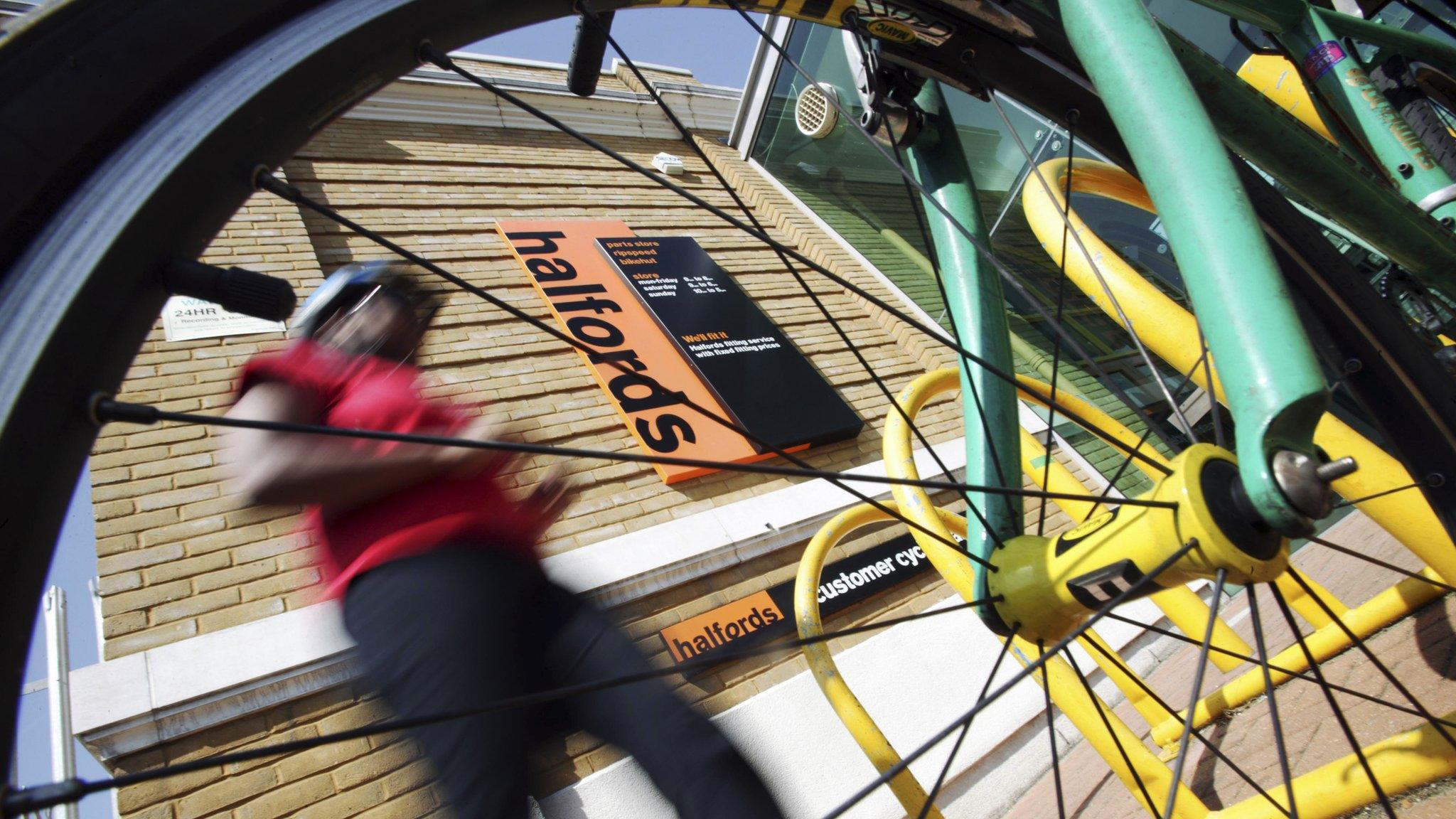 A cyclist walking to his bike outside a Halfords store.