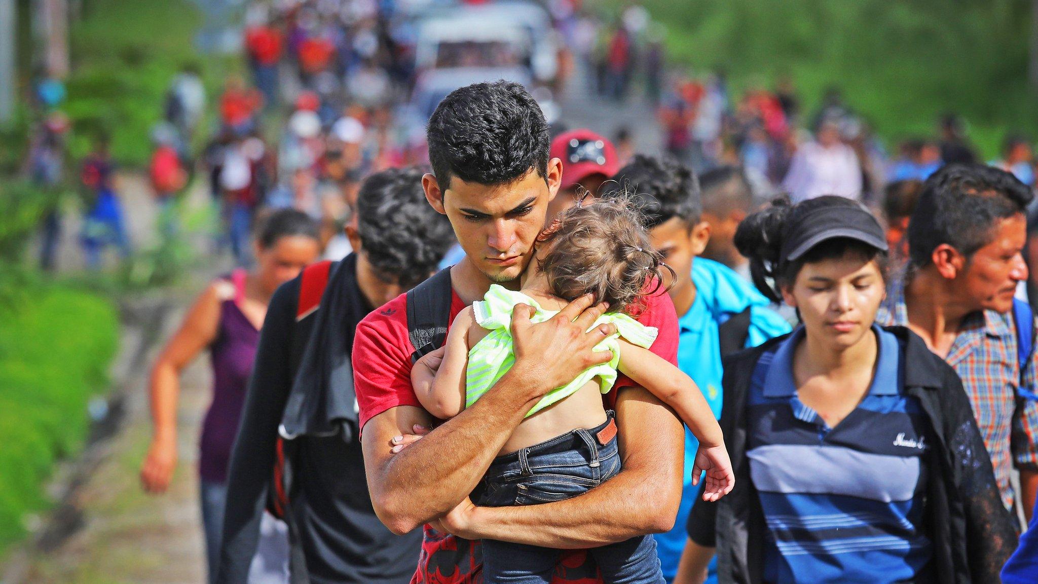 A man holds a baby as he walks with a large group of people