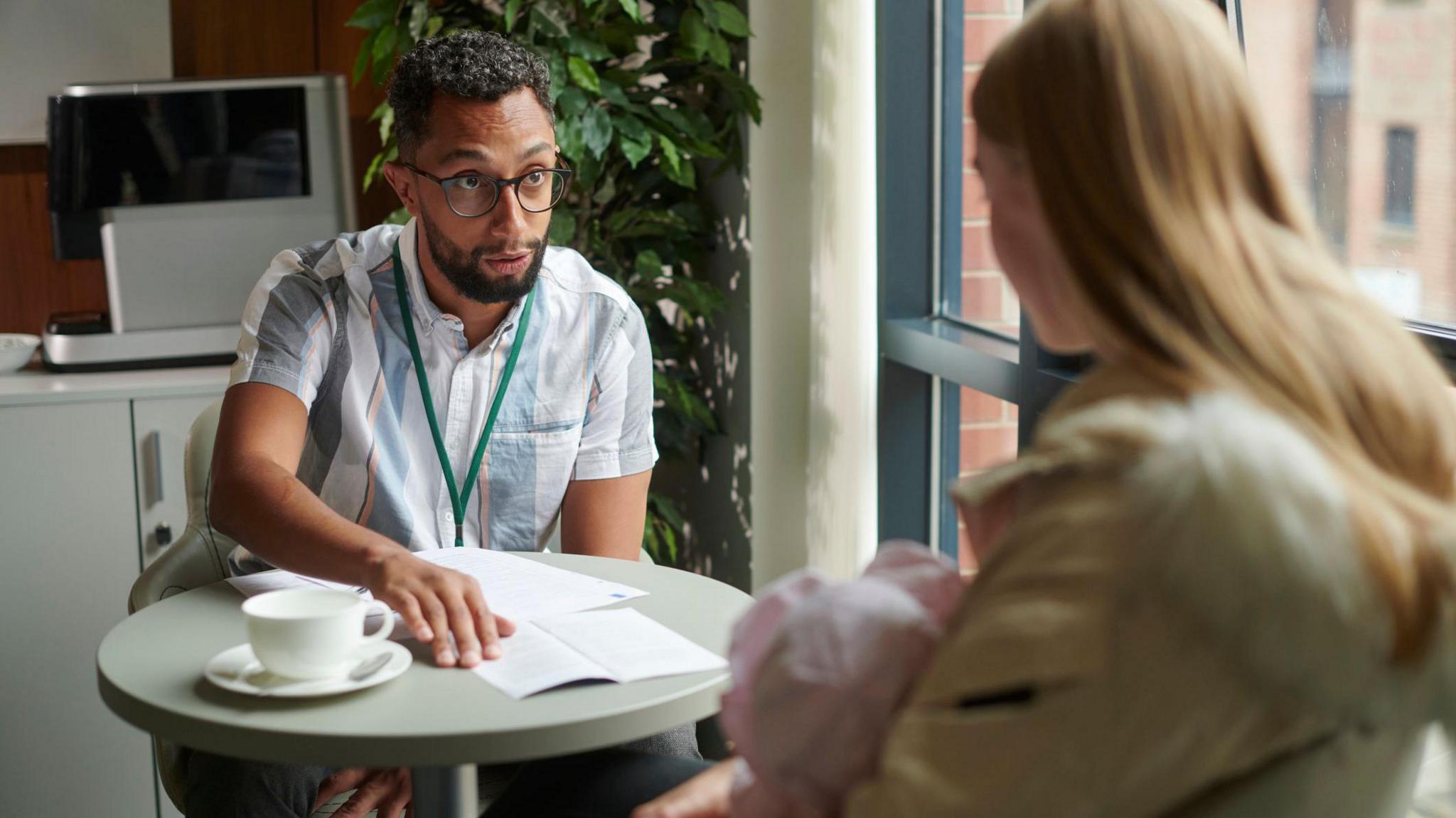 Young mother holds a baby while being shown paperwork by a man who appears to be an adviser