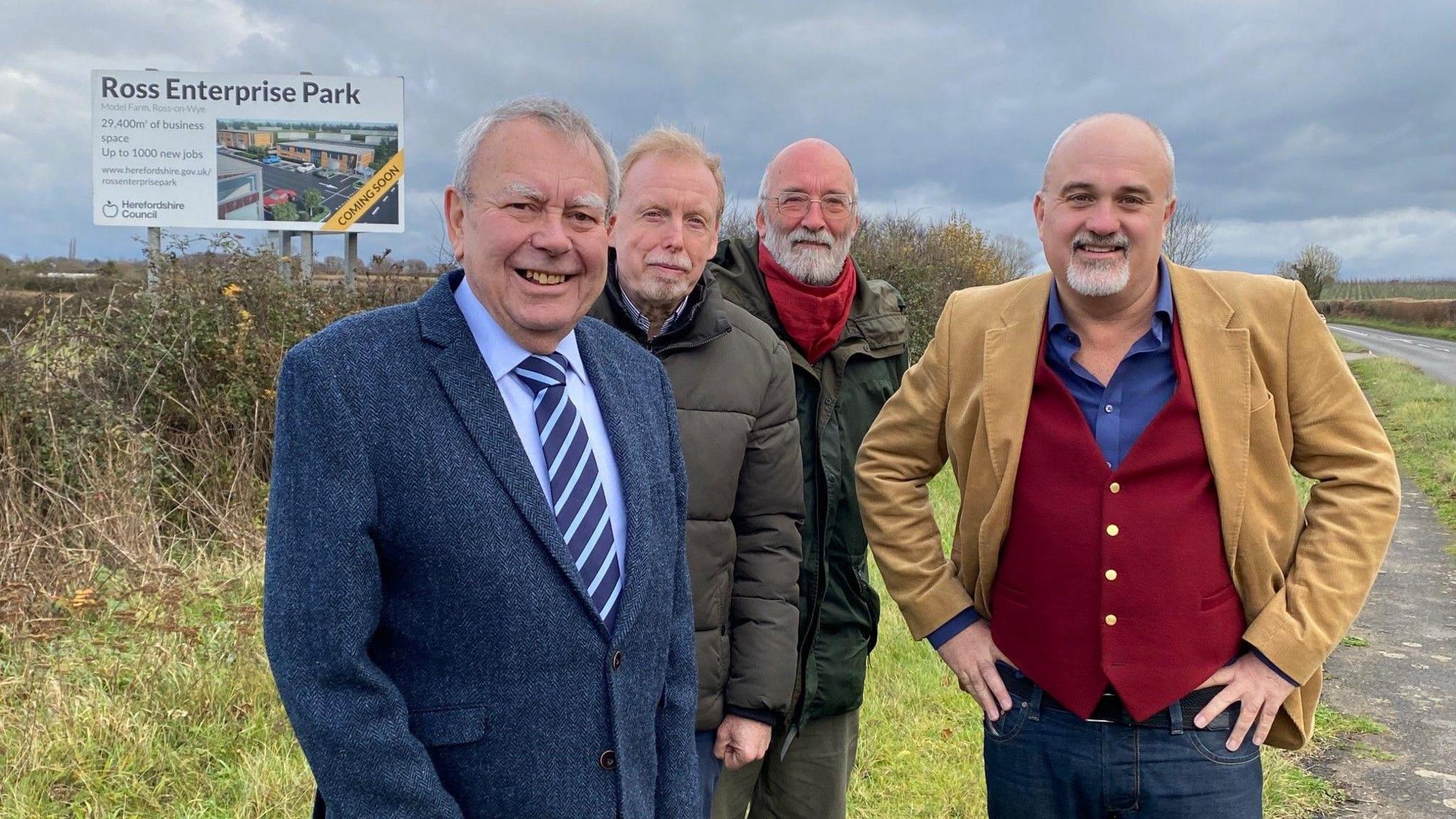 Four men standing outside in a field, with a large sign behind them that says 'Ross Enterprise Park'.