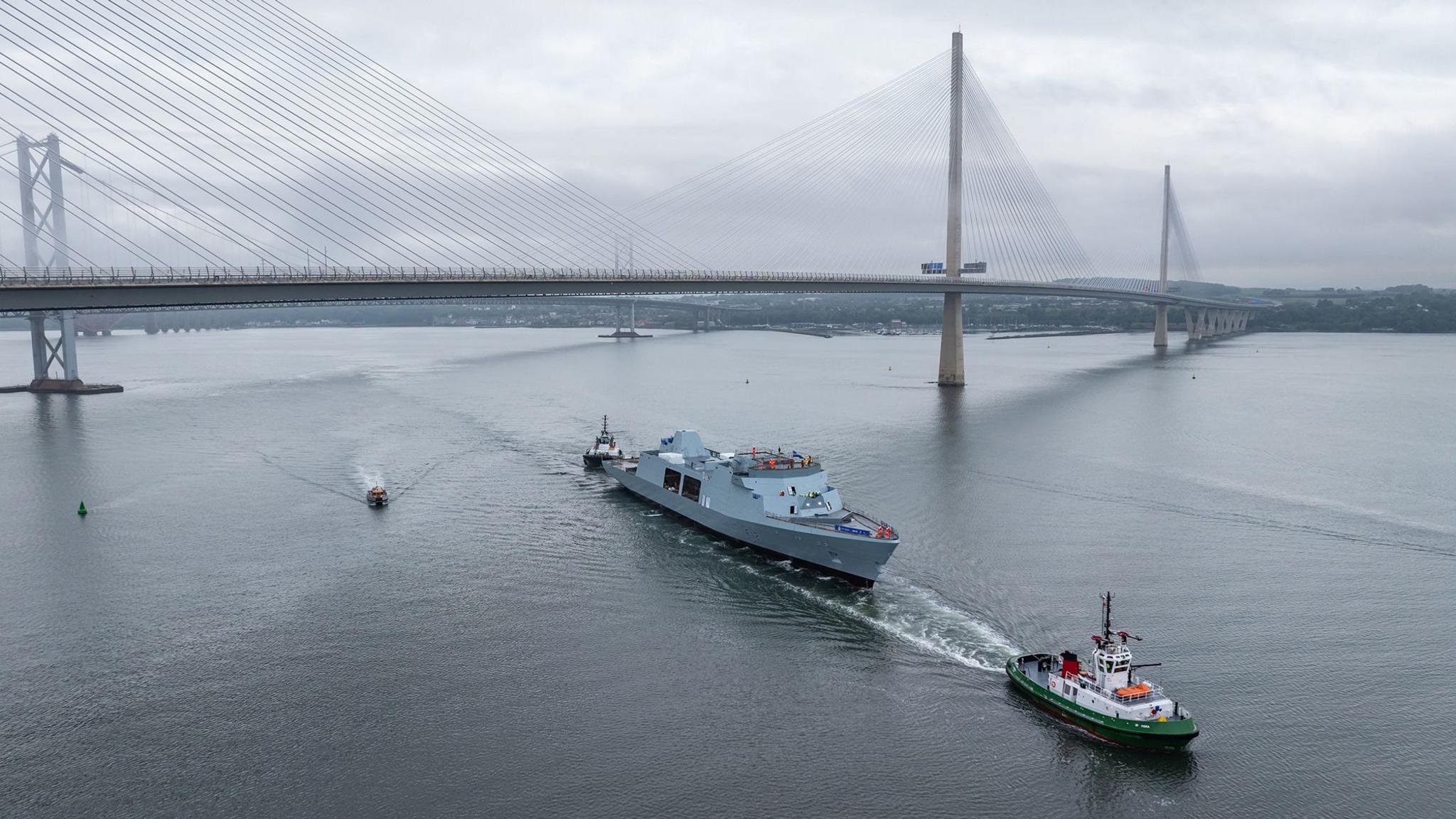A large naval ship passes under the Queensferry Crossing in the Firth of Forth