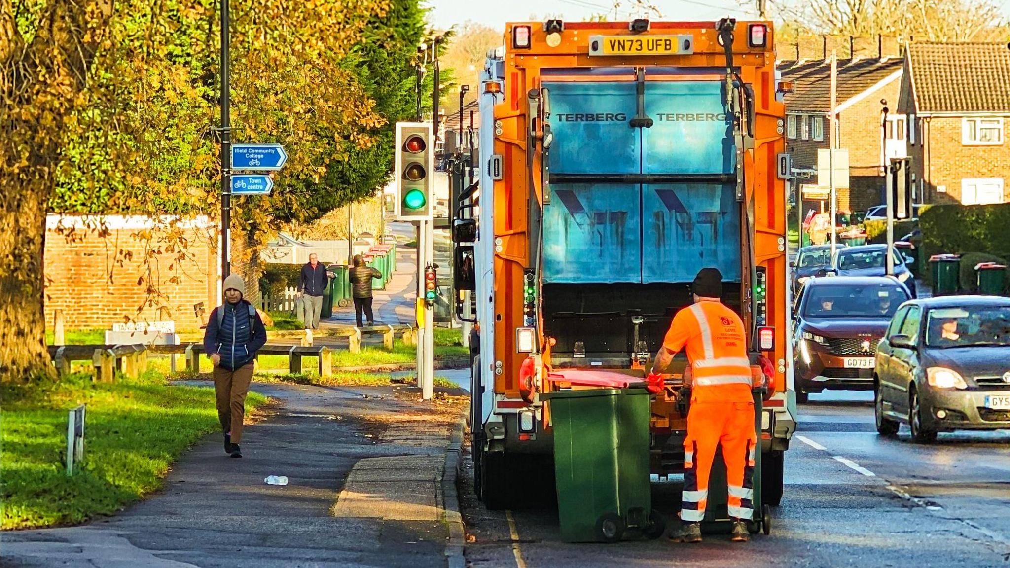 A refuse collection worker, wearing reflective workwear, emptying a rubbish bin into the rubbish truck on a city street.