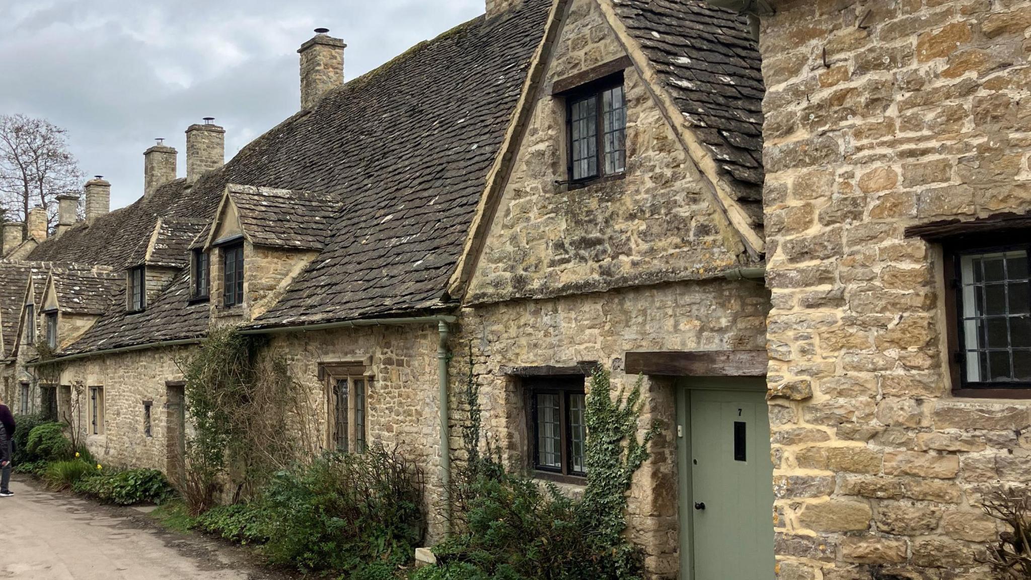 Arlington Row in Bibury - a row of stone cottages with greenery and a stream running in front of them.