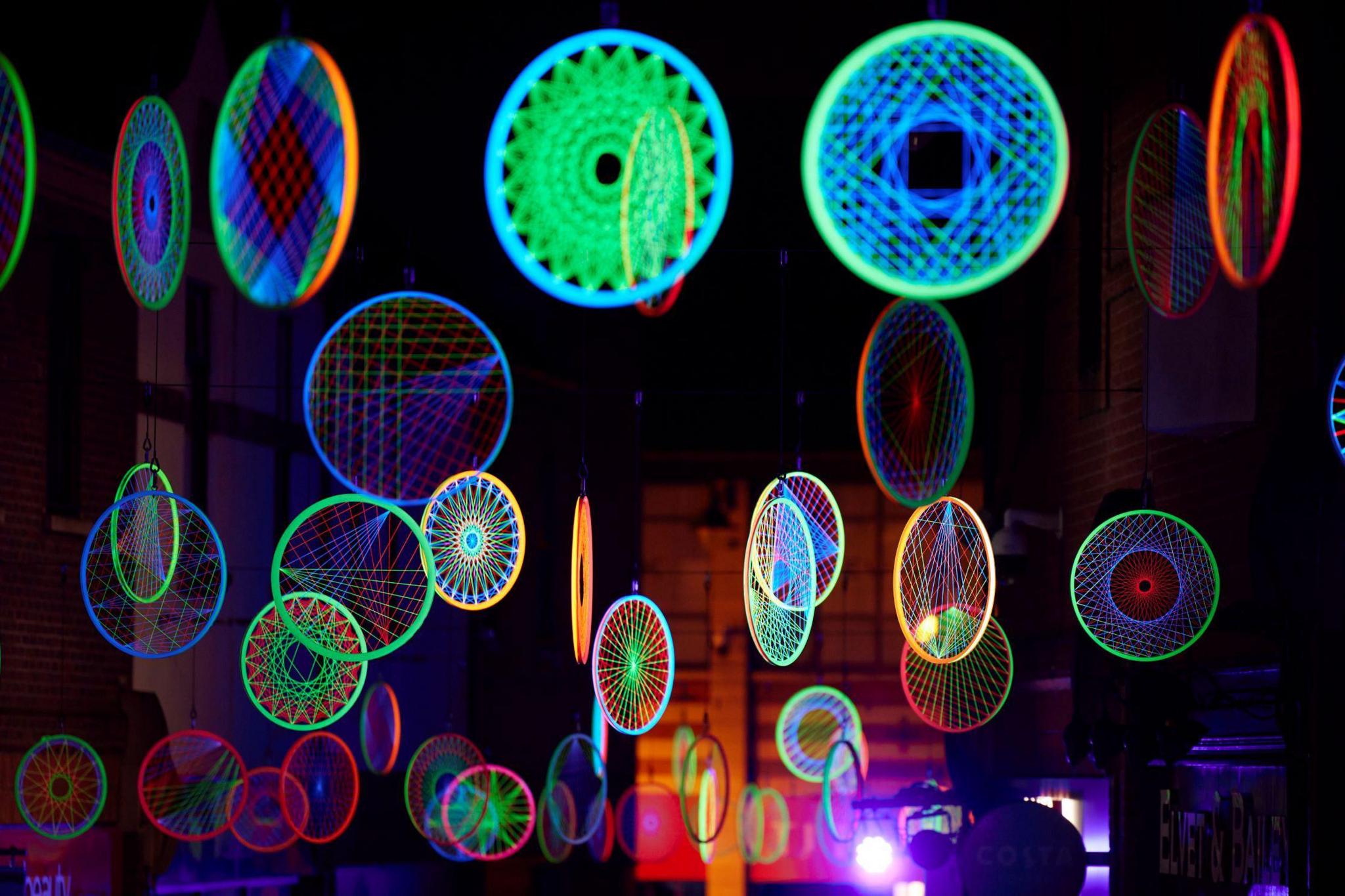 Dozens of wheels are suspended from the air and illuminated in different neon colours.