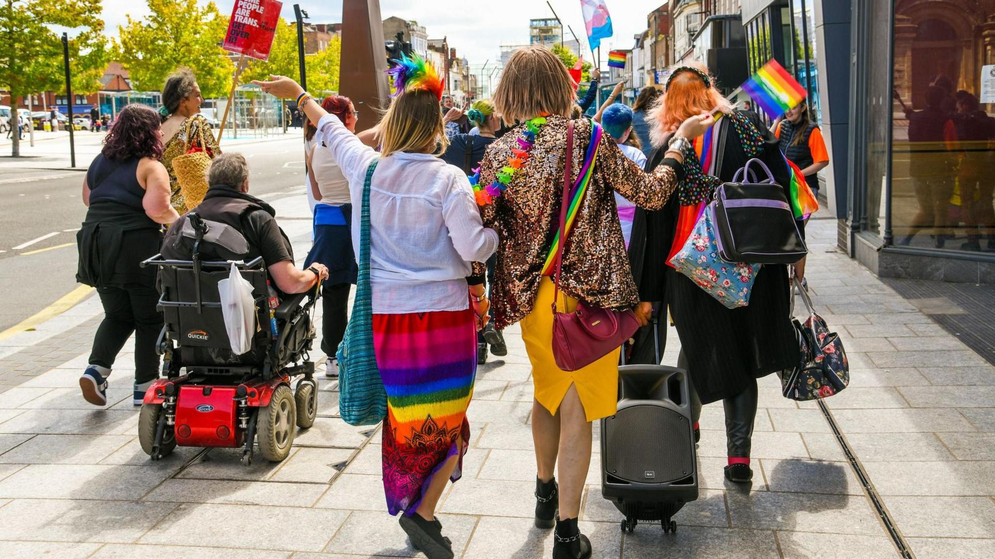 A group of people waving rainbow flags walk down a street